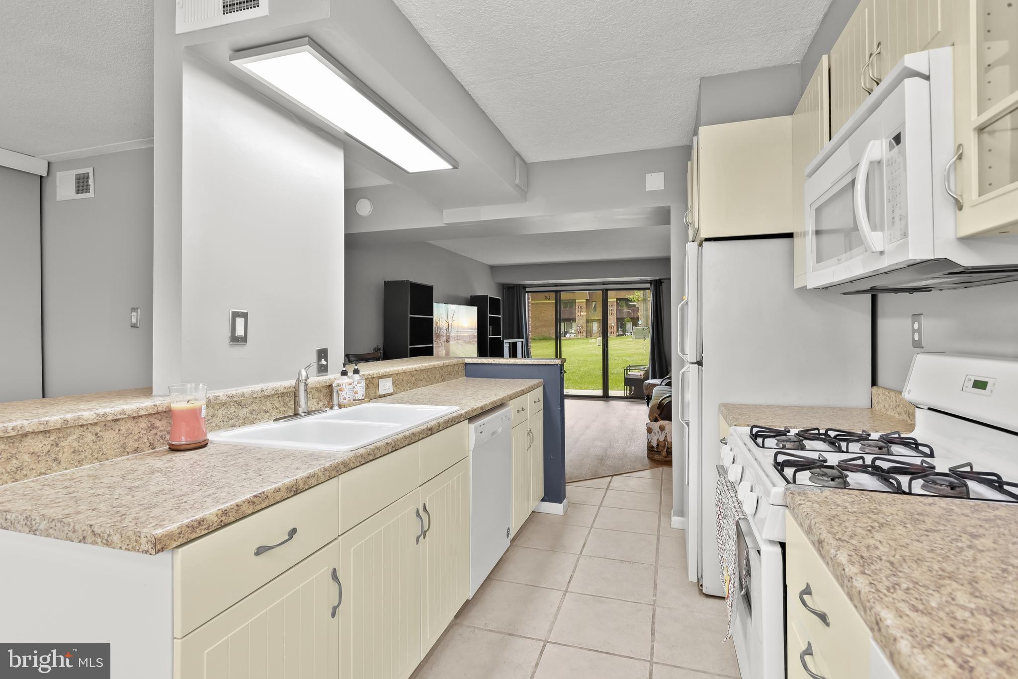 Kitchen with cream cabinets and speckled counters, opening to a living area with sliding glass doors.