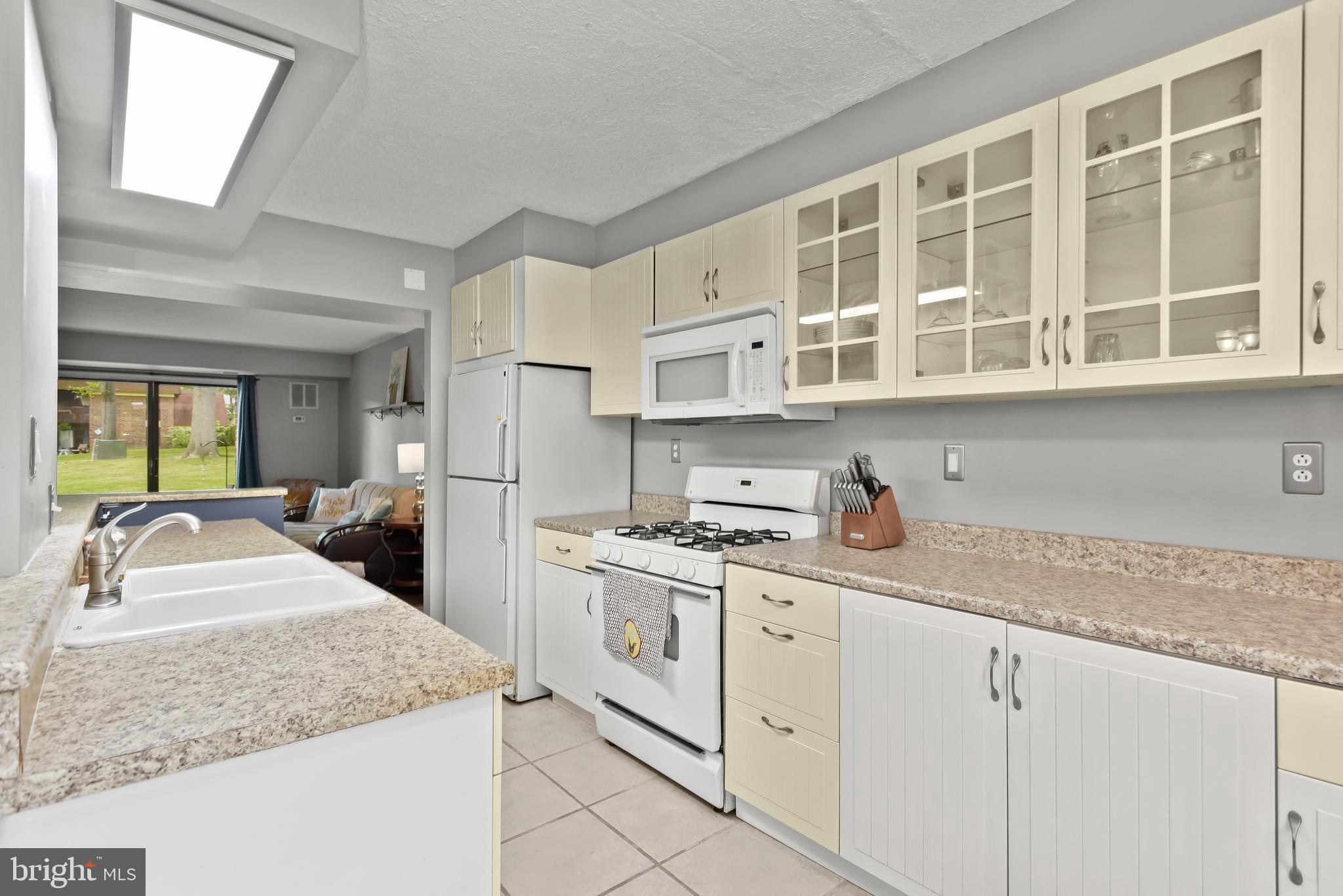 Kitchen with cream cabinets, stone-look counters, white appliances, and a view into the living area.