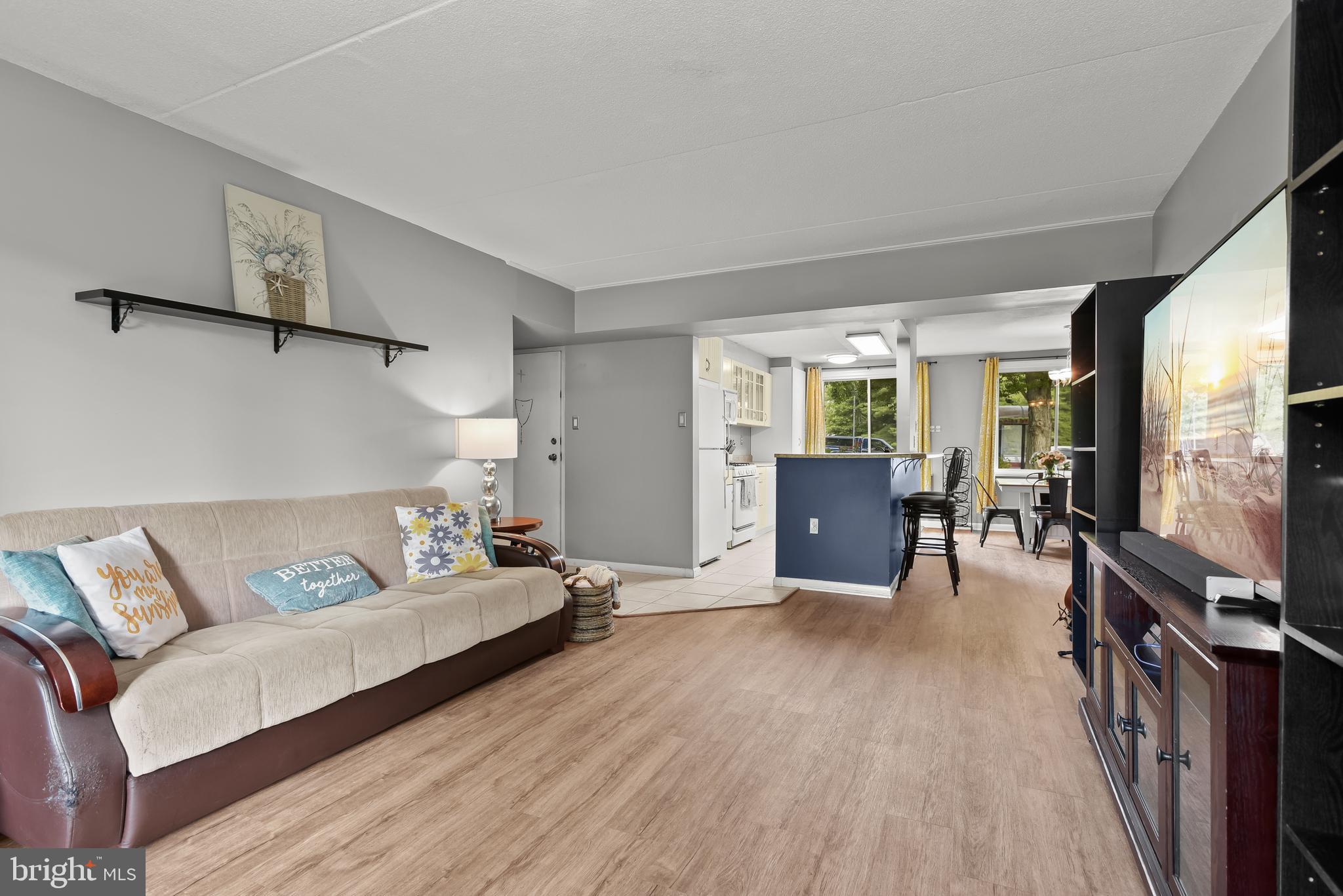 Open-plan living room with a beige sectional, wood-look floors, and a blue kitchen island.