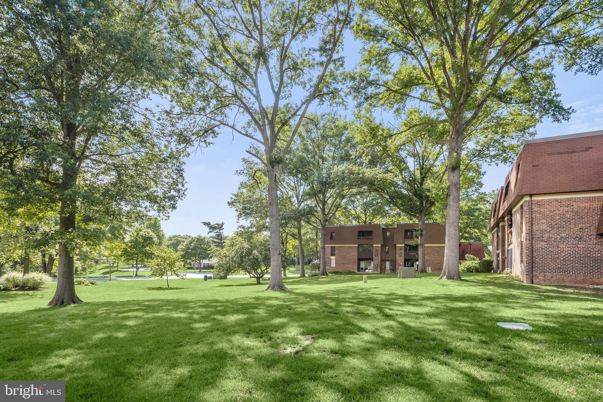 Brick condominium buildings set behind a green lawn and mature trees.