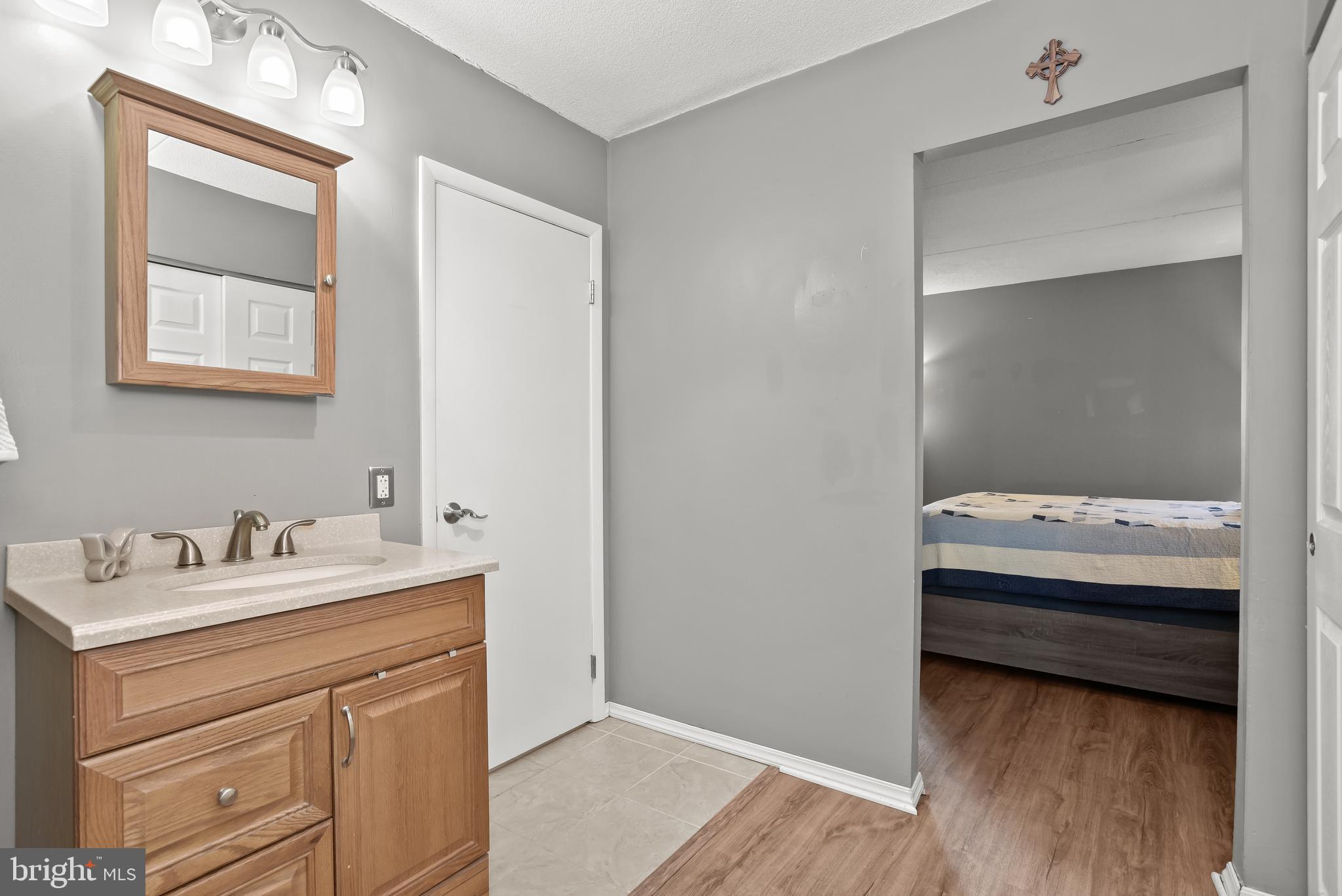 Bathroom vanity and mirror beside an open doorway to a bedroom with a striped bedspread.
