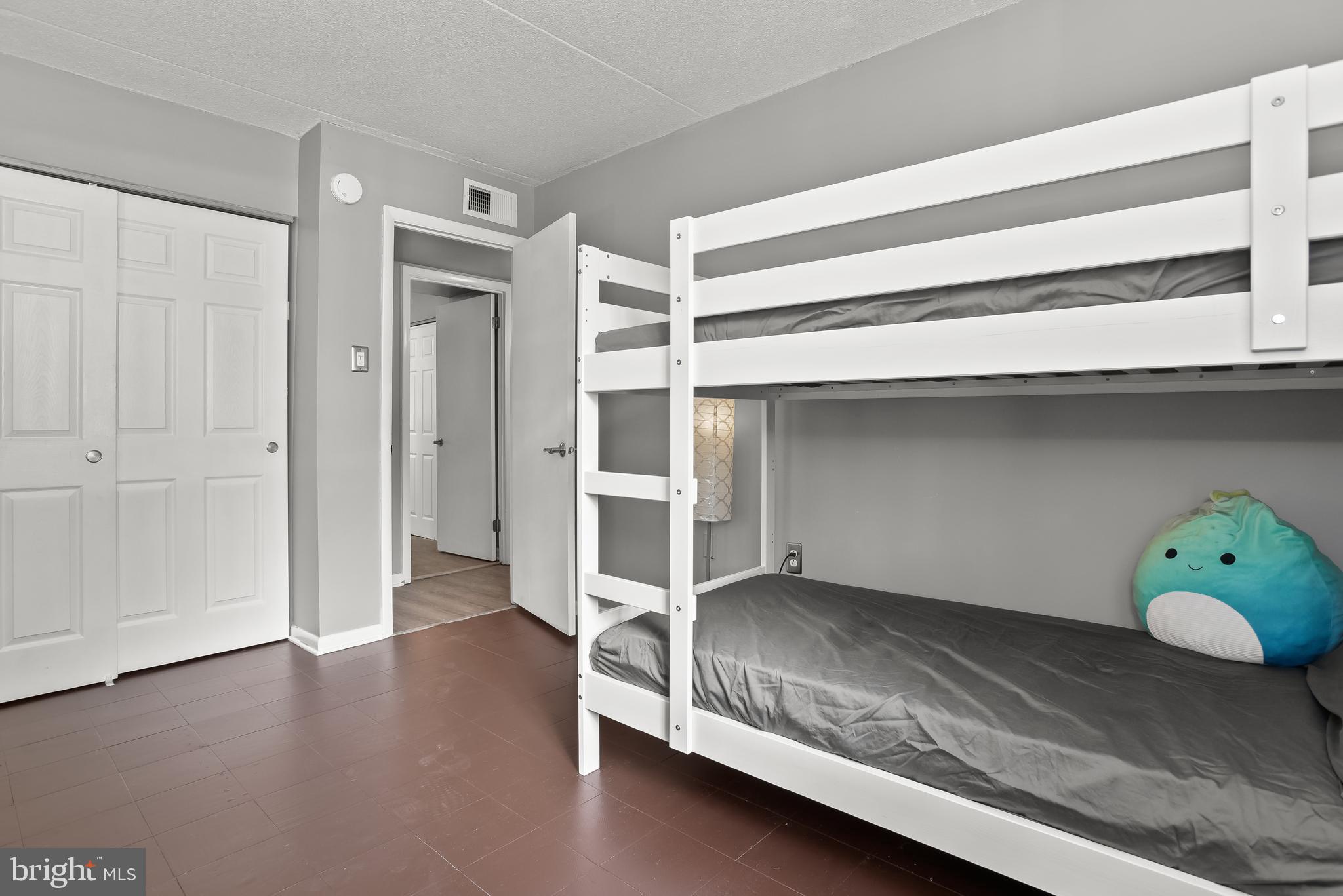 Bedroom with a white bunk bed, gray bedding, and a turquoise plush cushion.