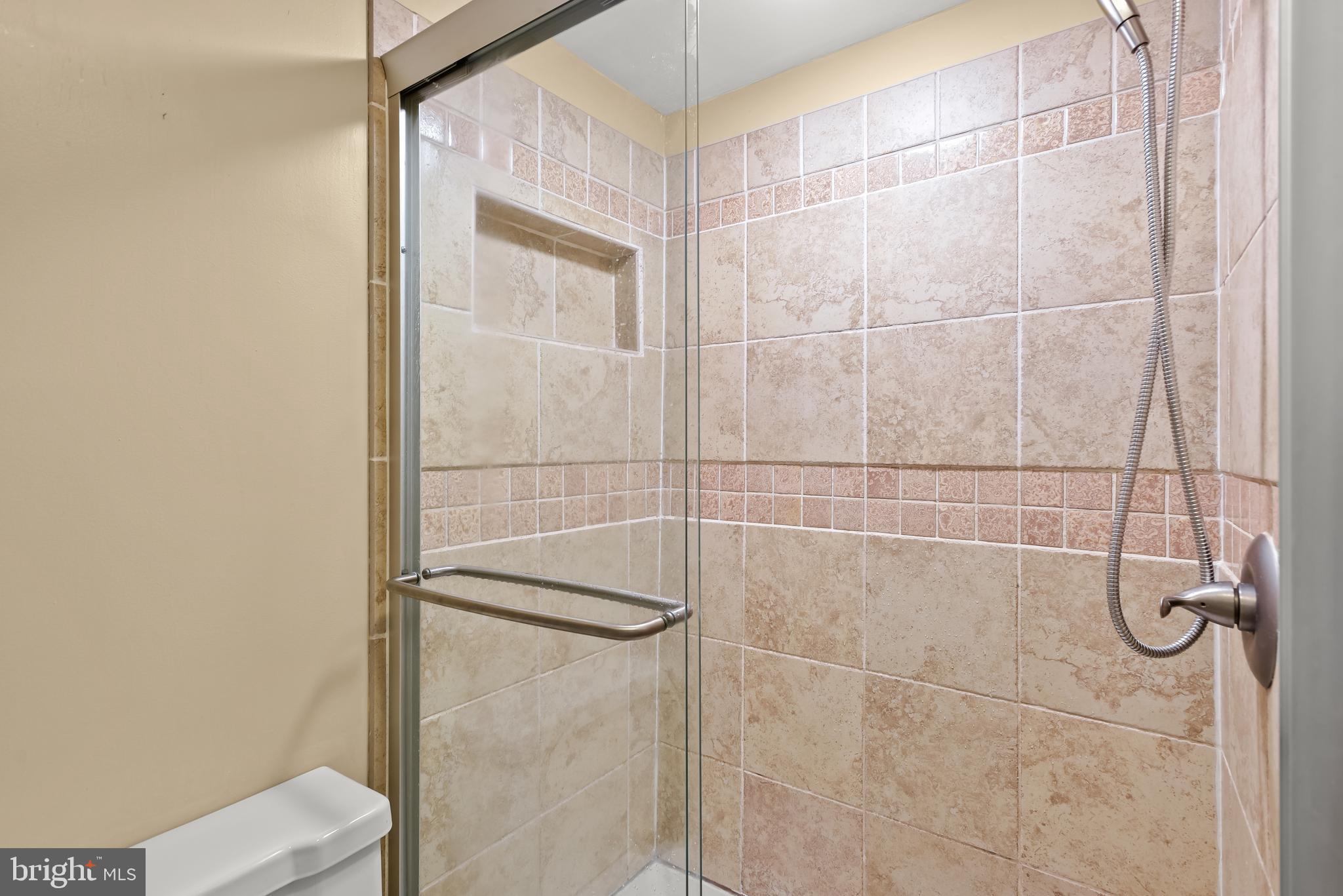 Tiled walk-in shower with a glass enclosure, built-in niche, and handheld showerhead.