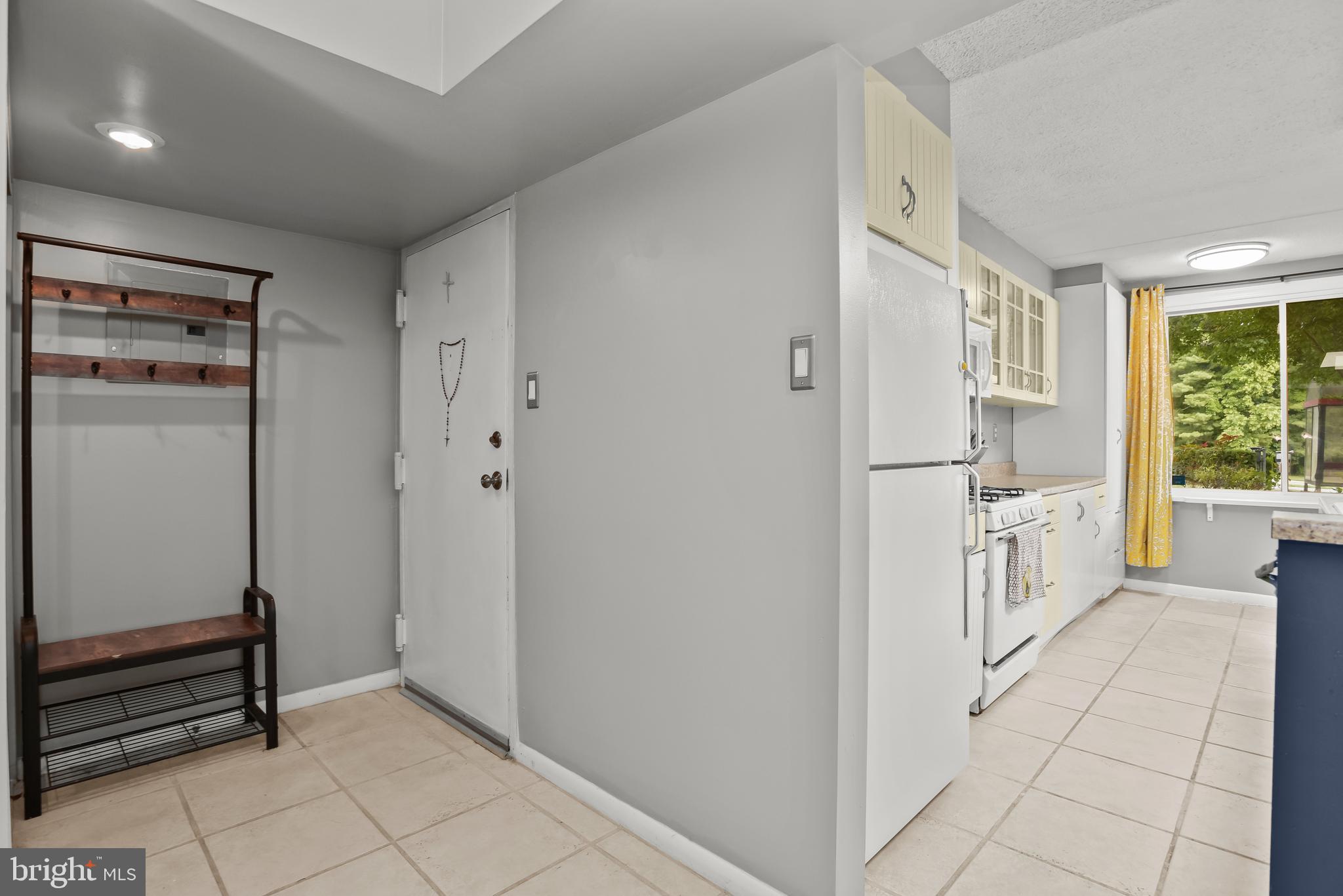 Condo entryway and kitchen with pale cabinets, white appliances, and a wooden coat bench.