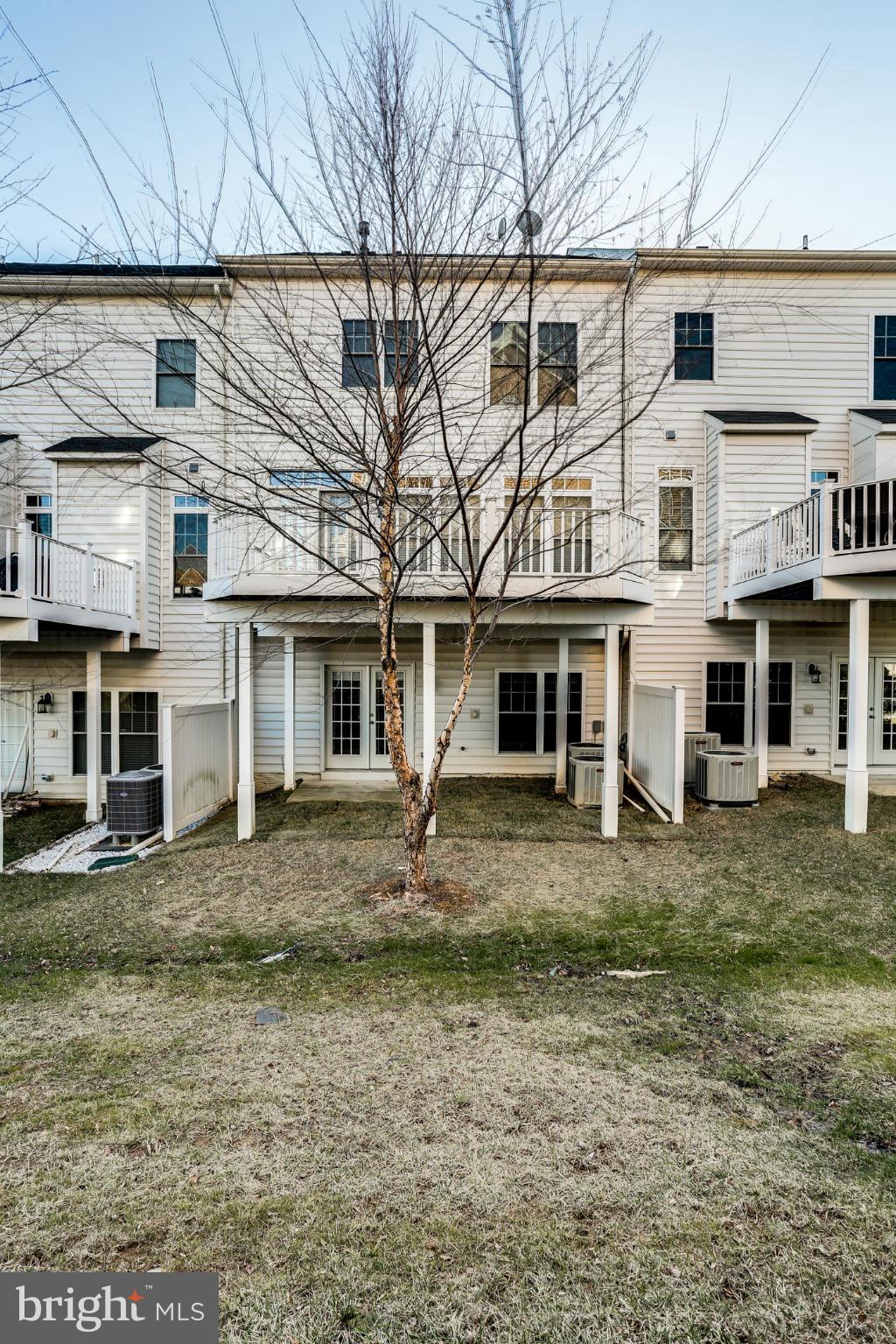 Rear of a white-sided townhouse with raised decks and a leafless tree in the yard.