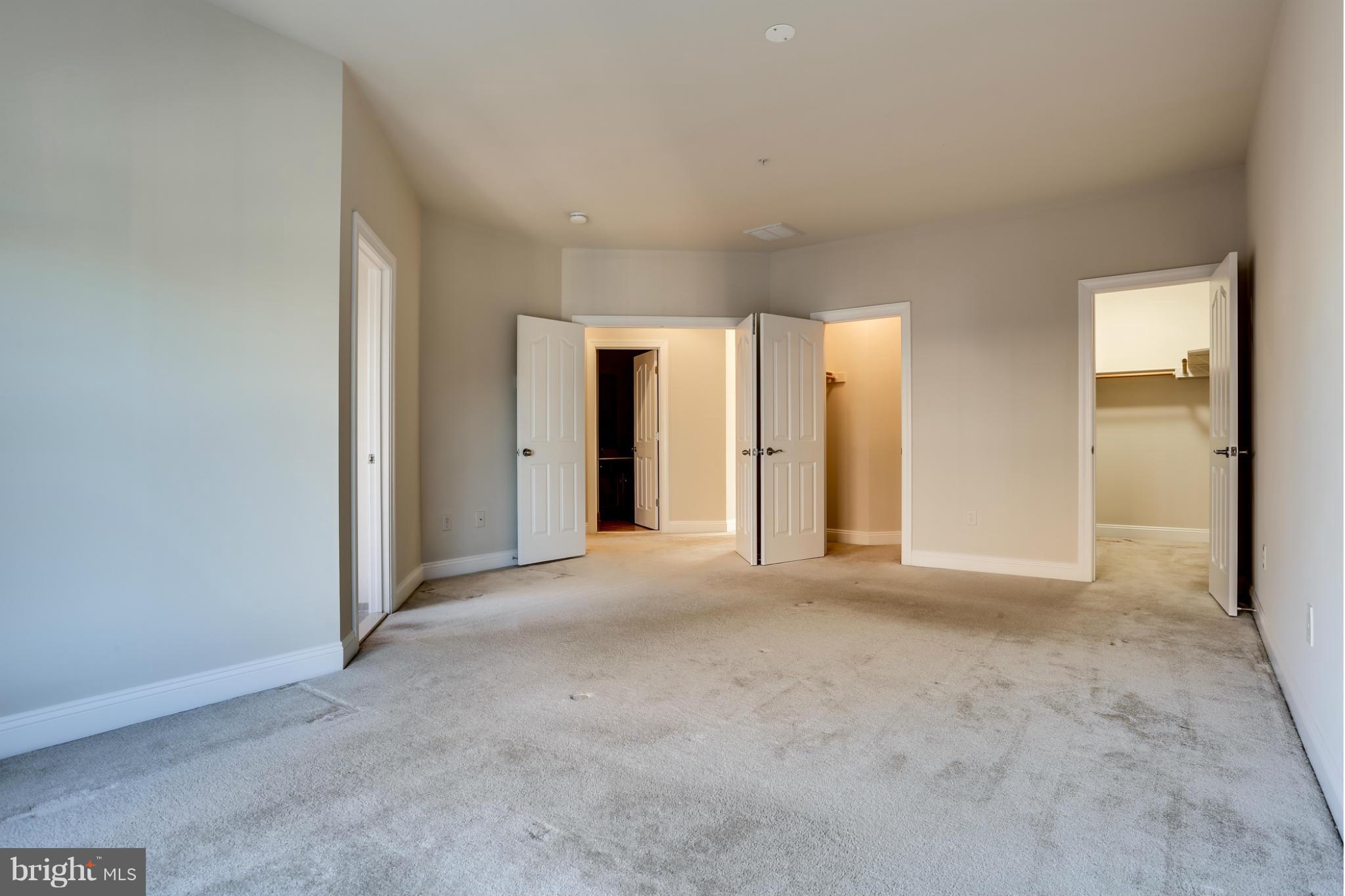 Vacant bedroom with light gray carpet and several open doors, including one to a closet.