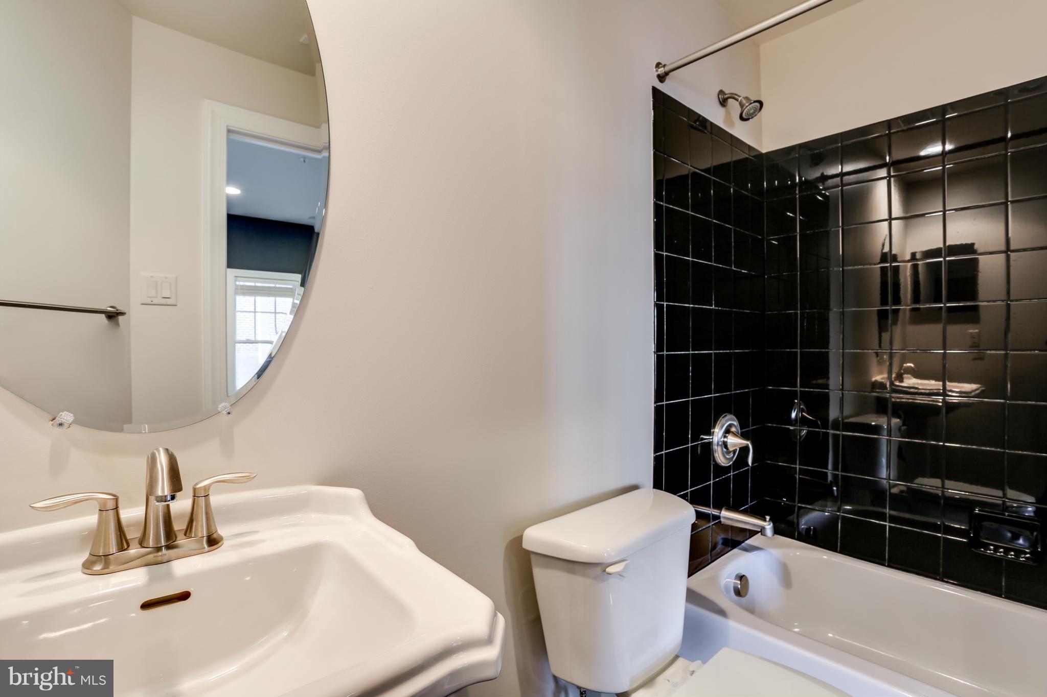 Bathroom with a white vanity, toilet, and bathtub lined with glossy black tile.