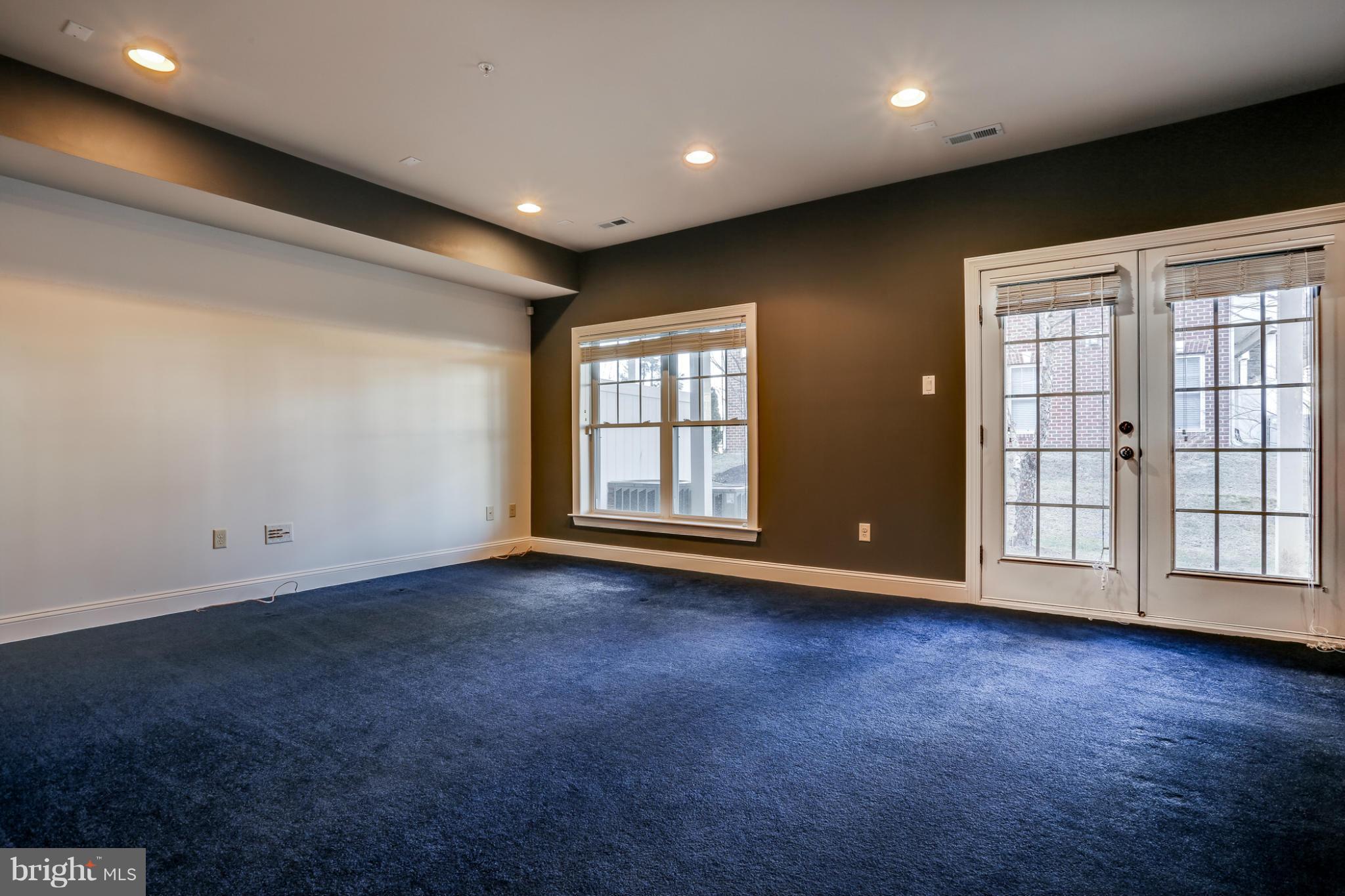 Empty room with blue carpet, a large window, and double glass doors with blinds.