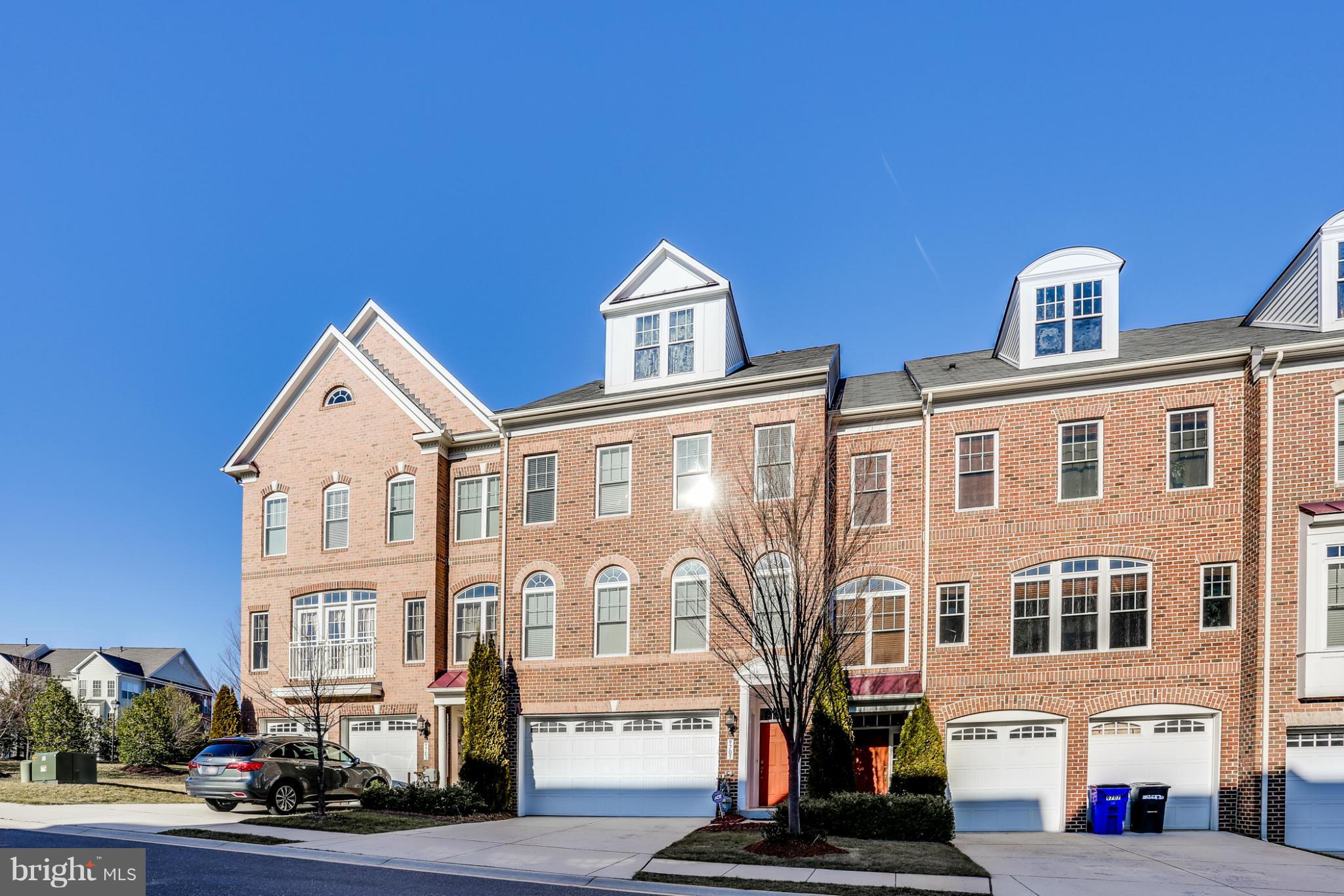 Red-brick townhouse with white dormers, an attached garage, and a red front door.