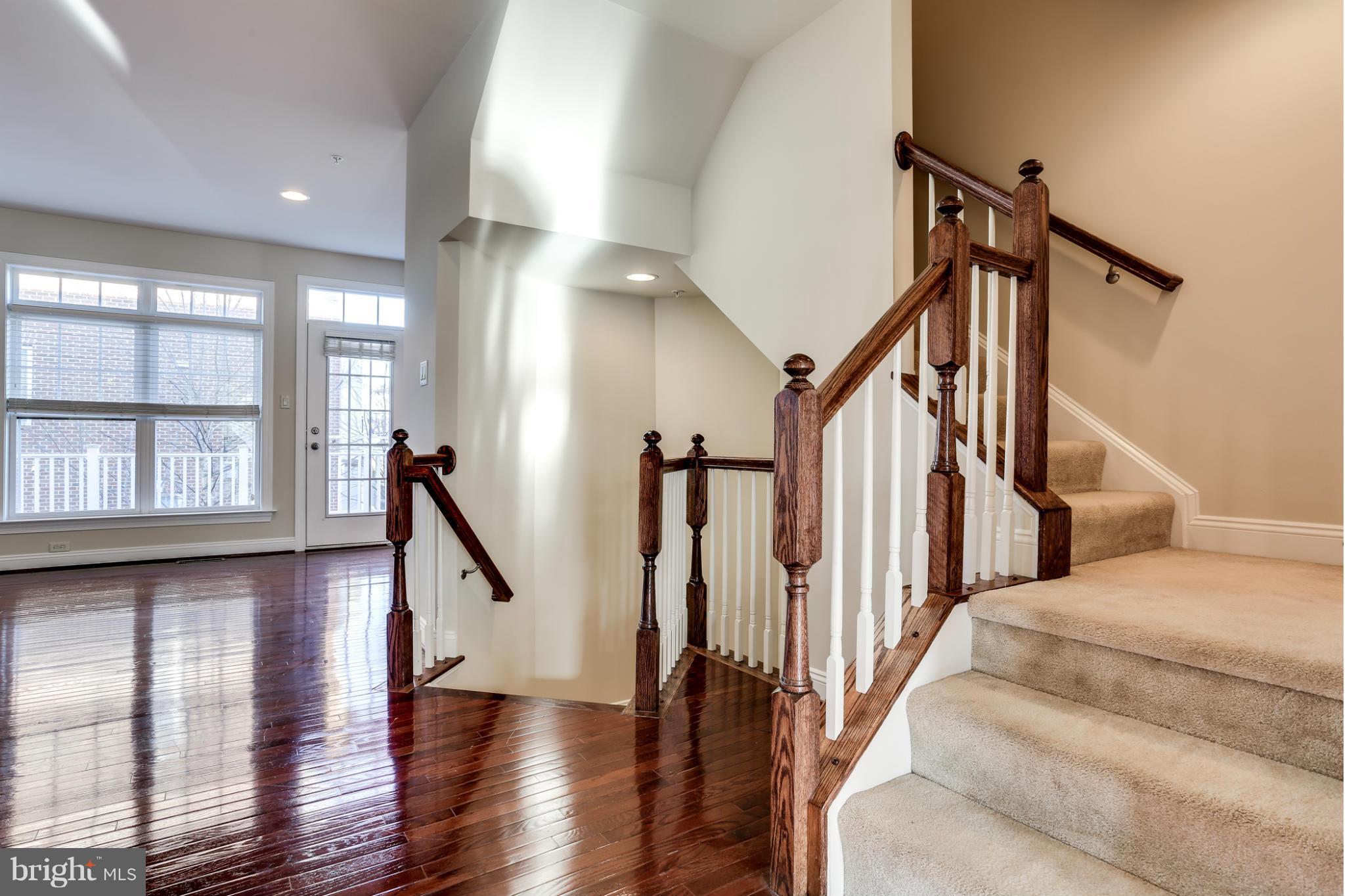 Foyer with glossy hardwood floors, large windows, and a carpeted staircase with dark wood railings.