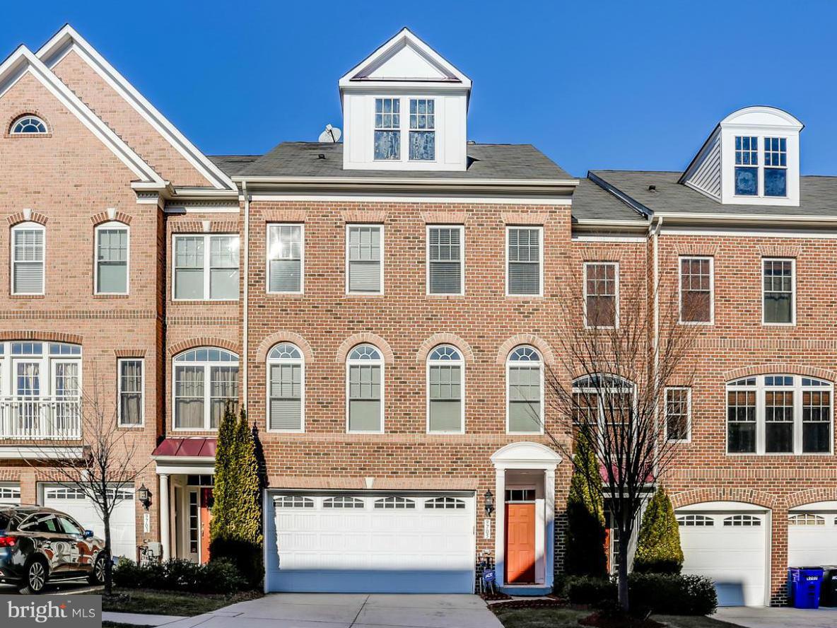 Brick townhouse with a white garage door, orange front door, and prominent roof dormers.