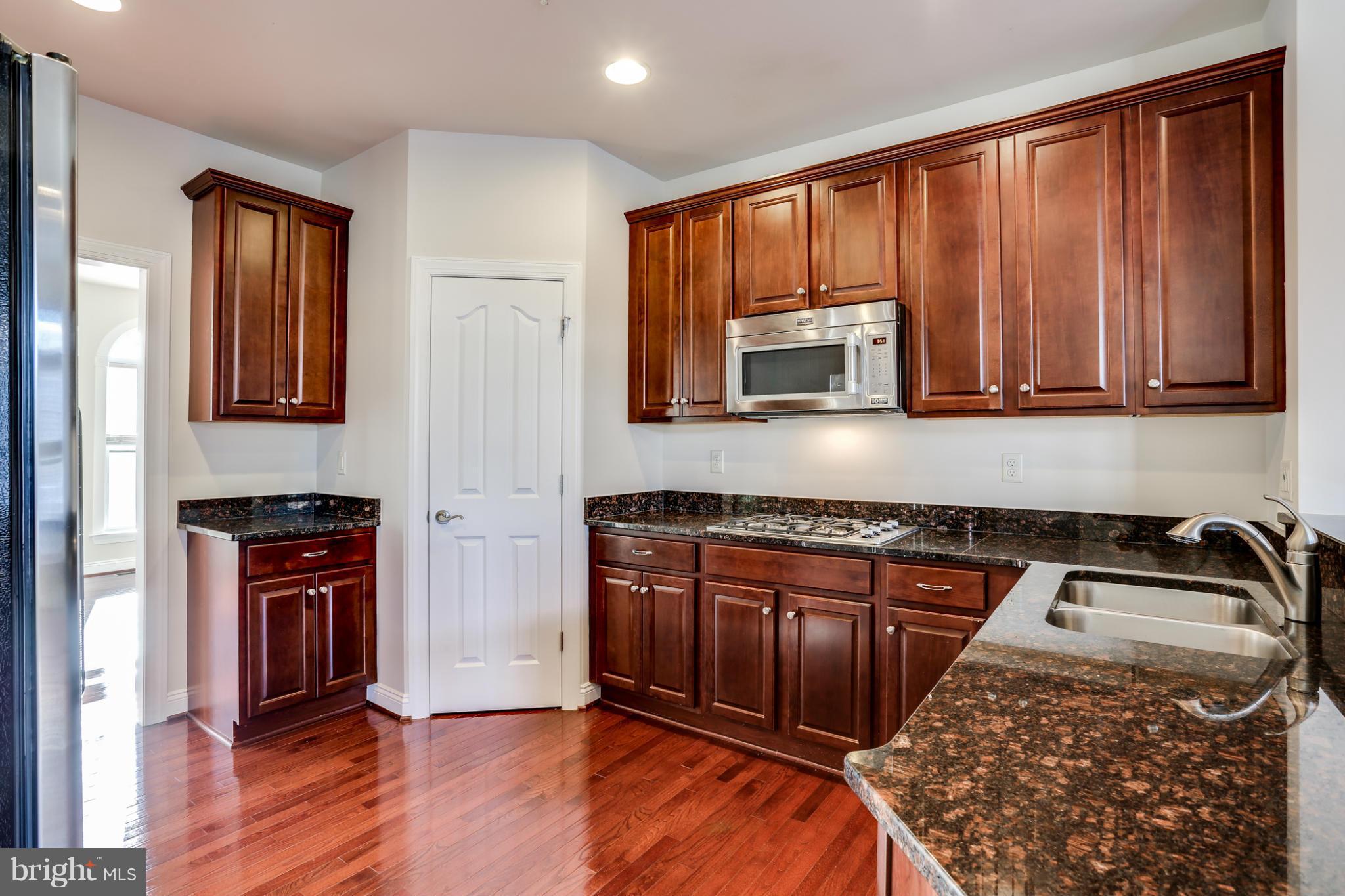 Kitchen with dark cherry cabinetry, granite counters, stainless microwave, gas cooktop, and hardwood floors.