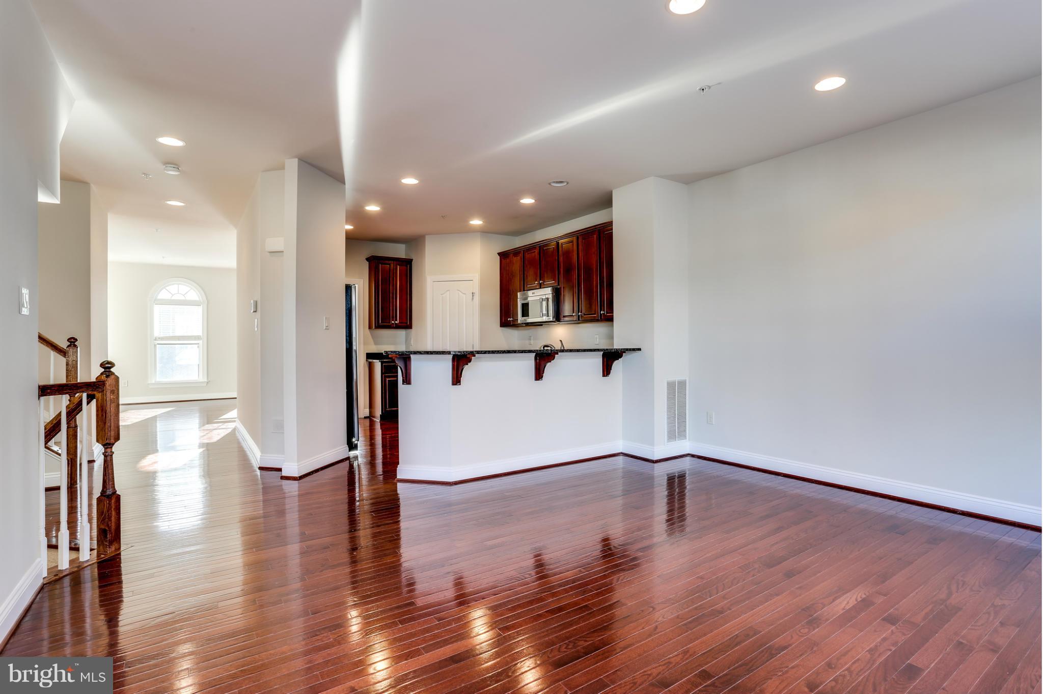 Unfurnished living area with glossy hardwood floors, dark kitchen cabinets, a breakfast bar, and an arched window.