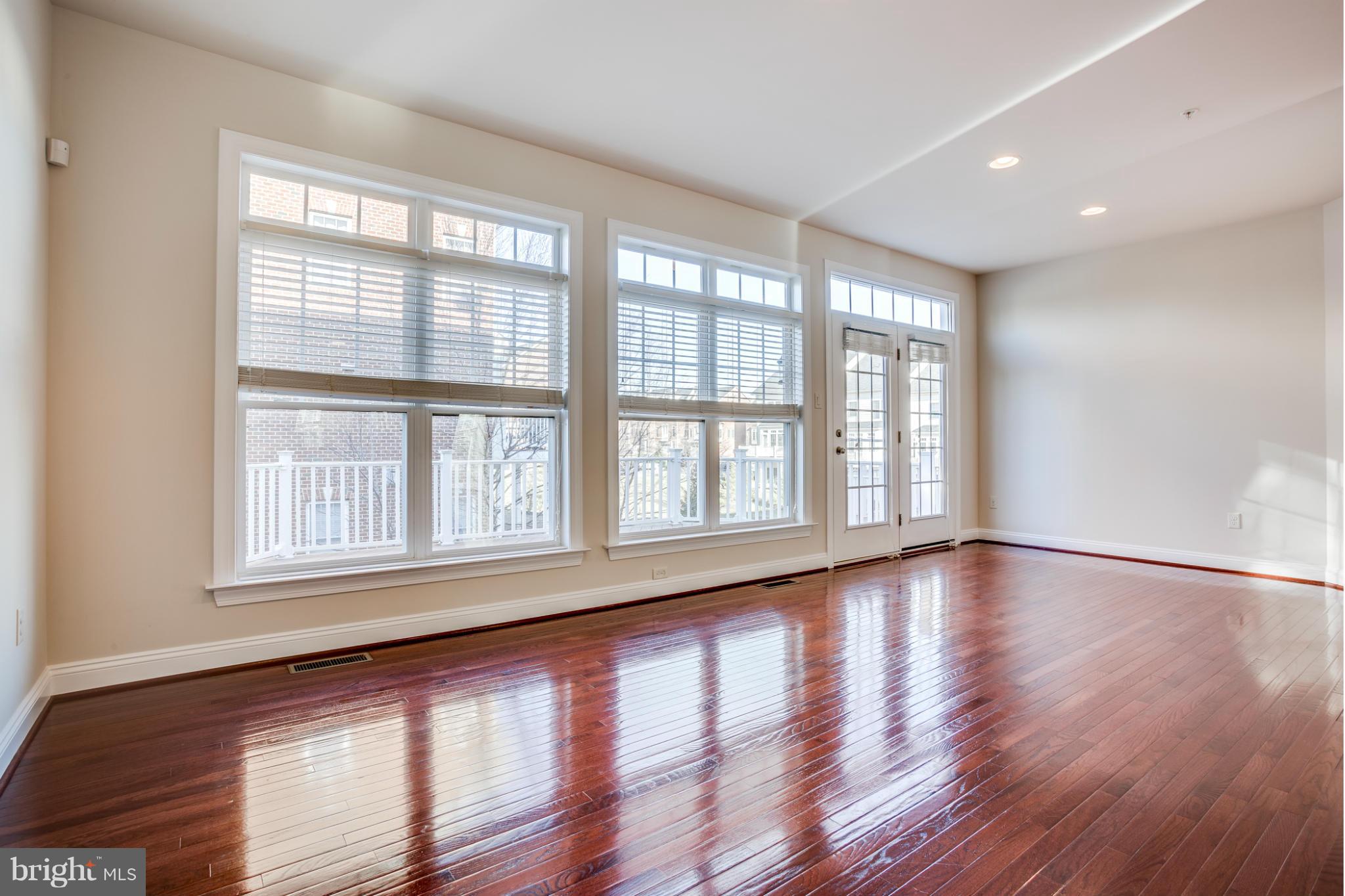 Empty living room with polished hardwood floors, large windows, and glass-paneled French doors.