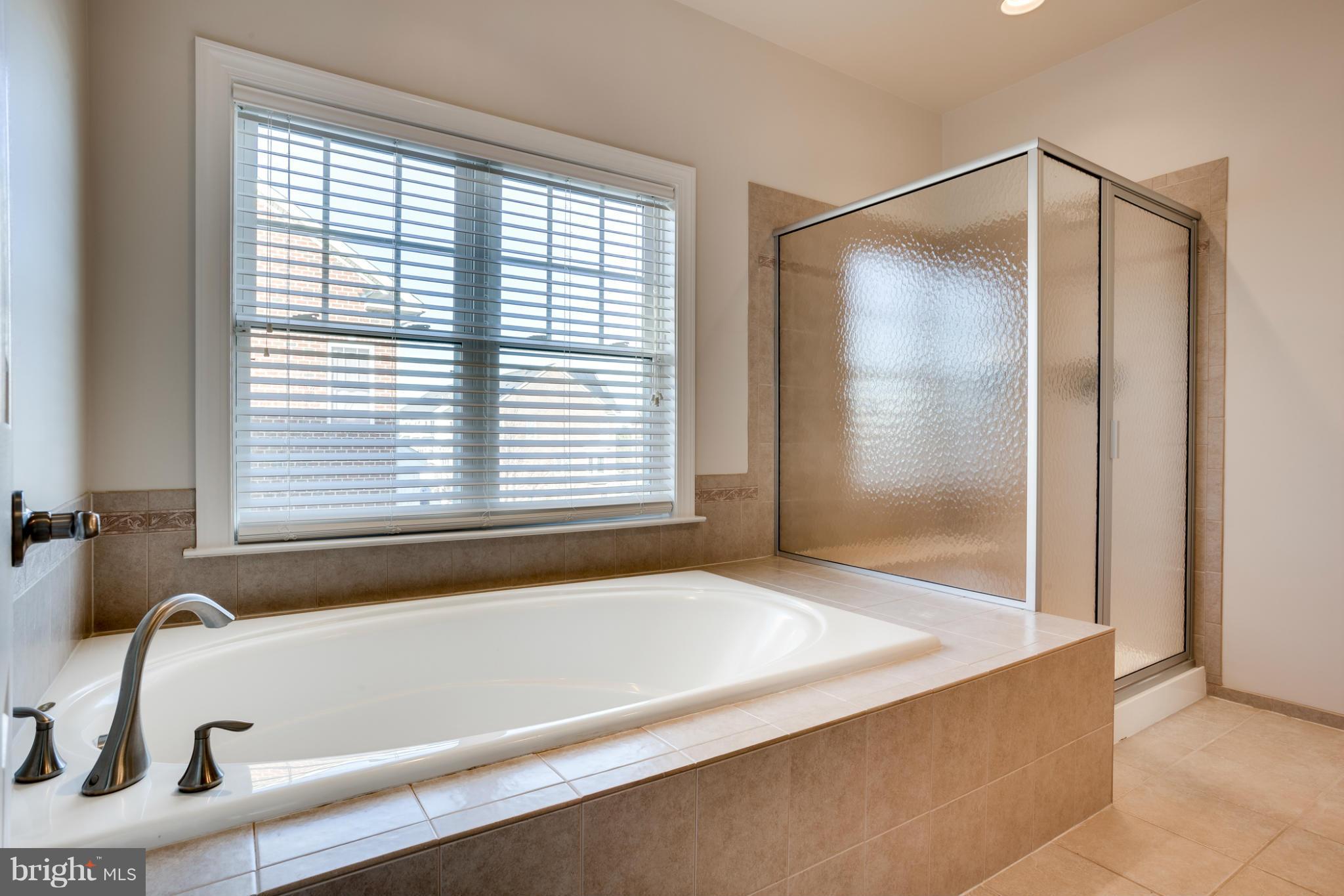 Bathroom with a tiled soaking tub beside a textured-glass shower and wide window.