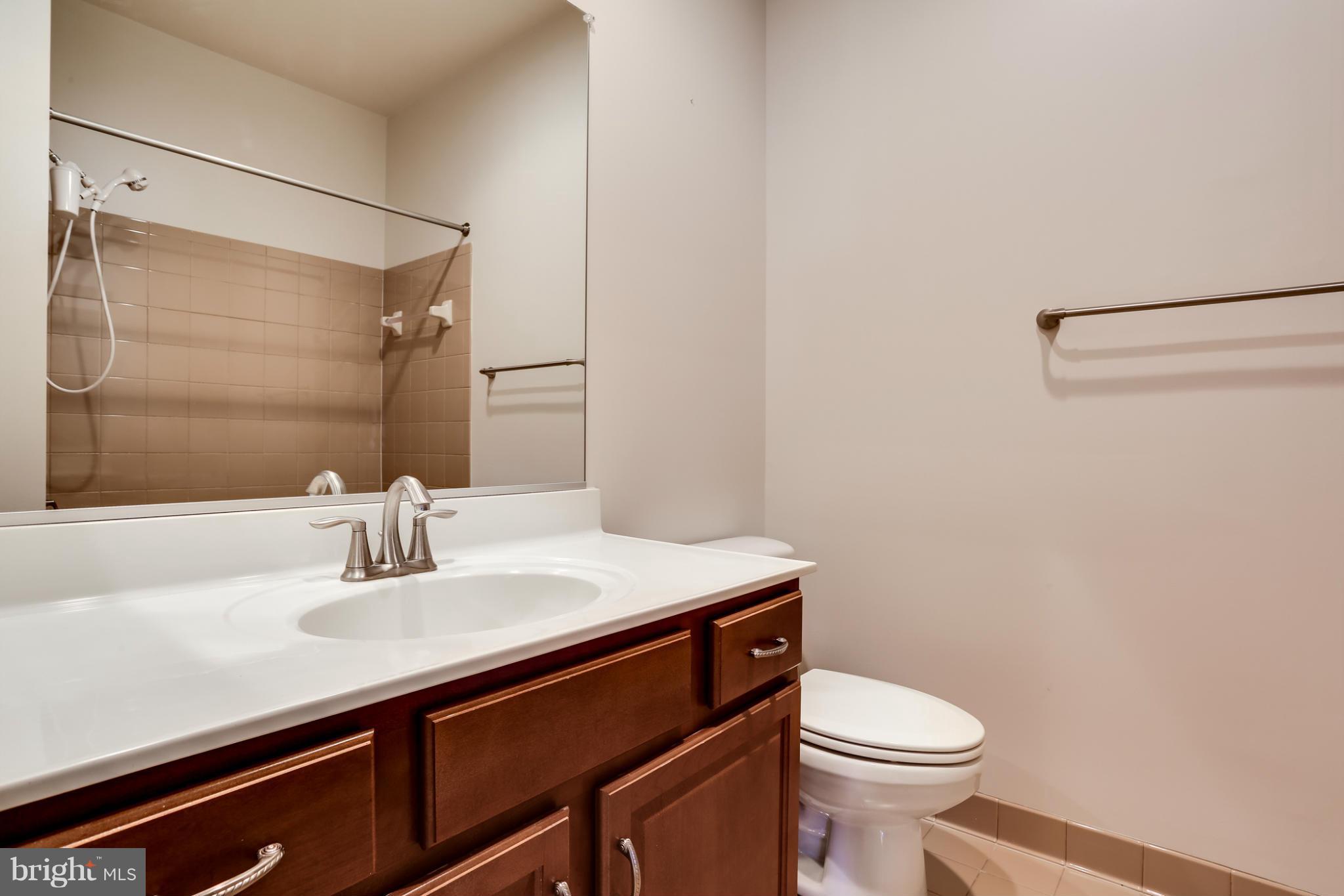 Bathroom with dark wood vanity, white sink counter, mirrored wall, tiled shower, and toilet.