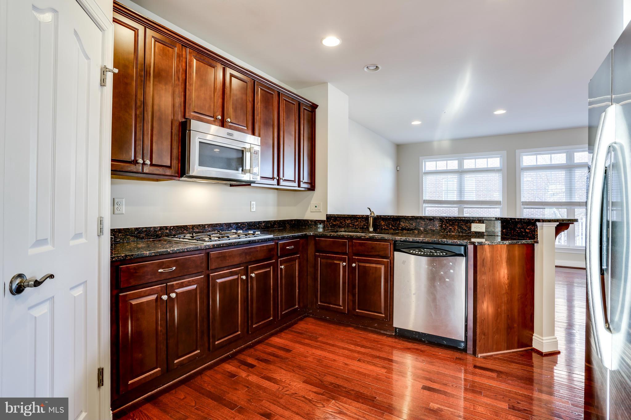 Kitchen with dark wood cabinets, granite countertops, stainless steel appliances, and hardwood floors.