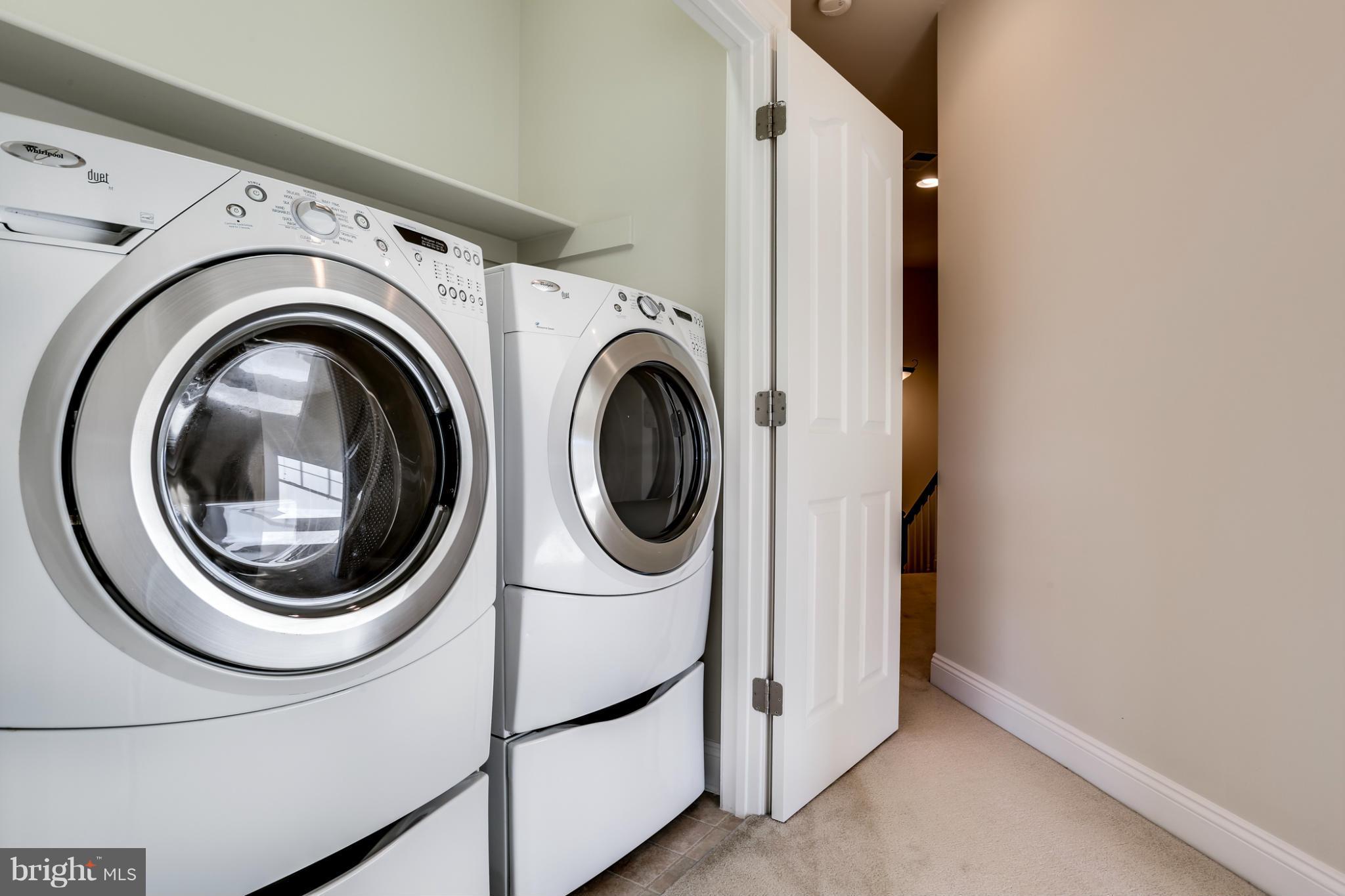 Laundry room with stacked white front-loading washer and dryer beside an open hallway door.