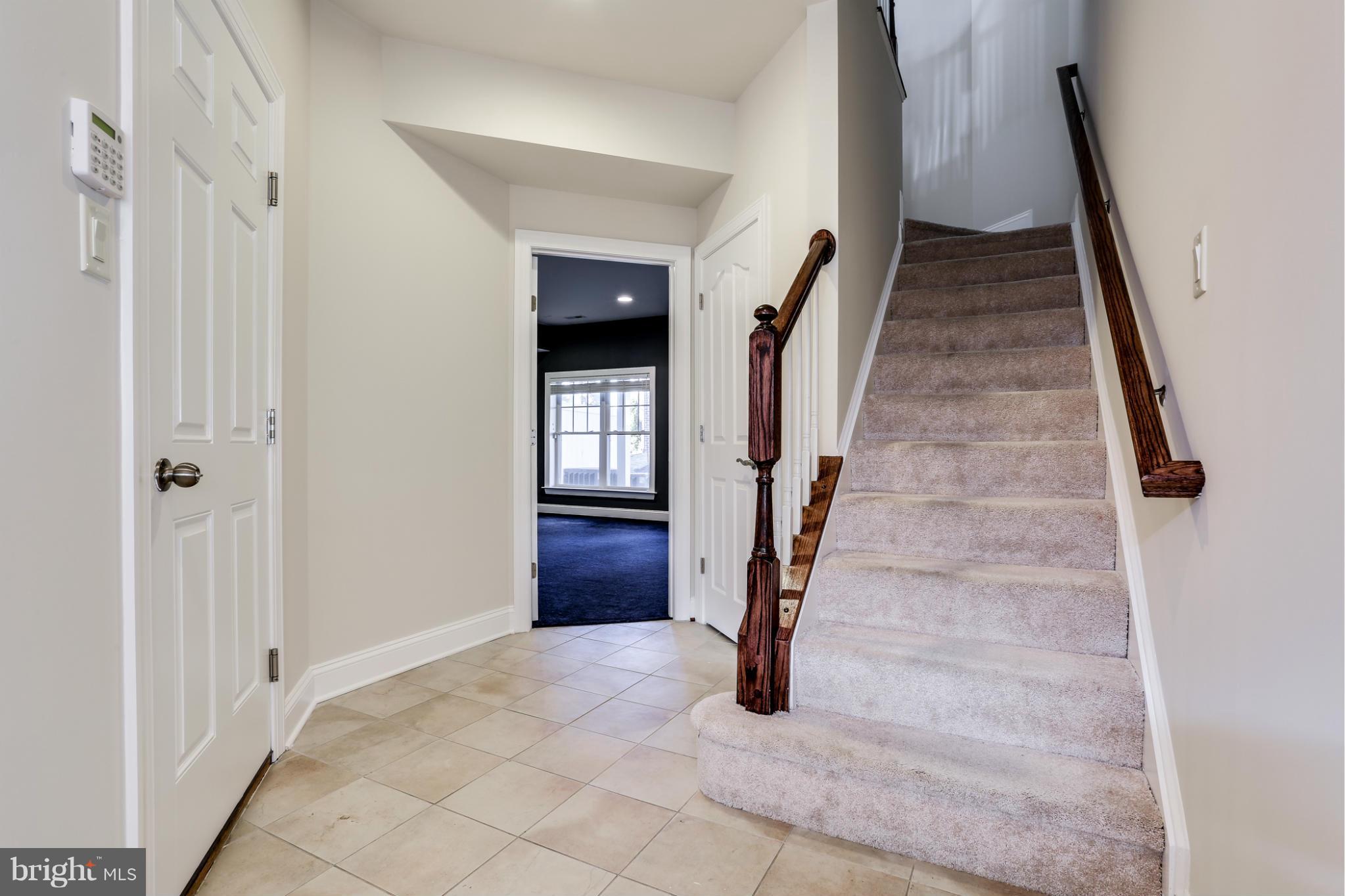Foyer with beige tile flooring, a carpeted staircase, and dark wood handrails.