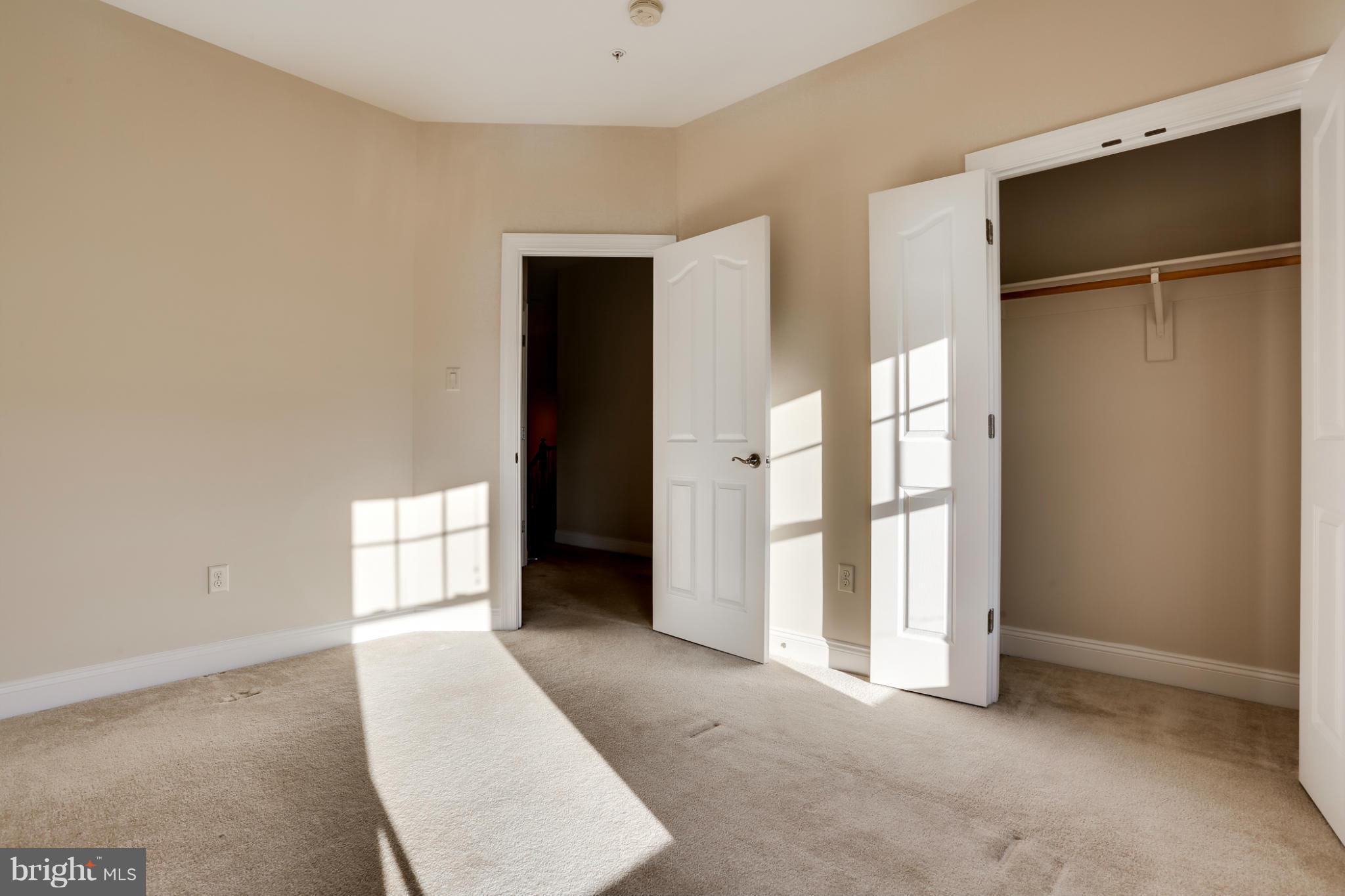 Empty carpeted bedroom with an open closet and bright sunlight across the floor.
