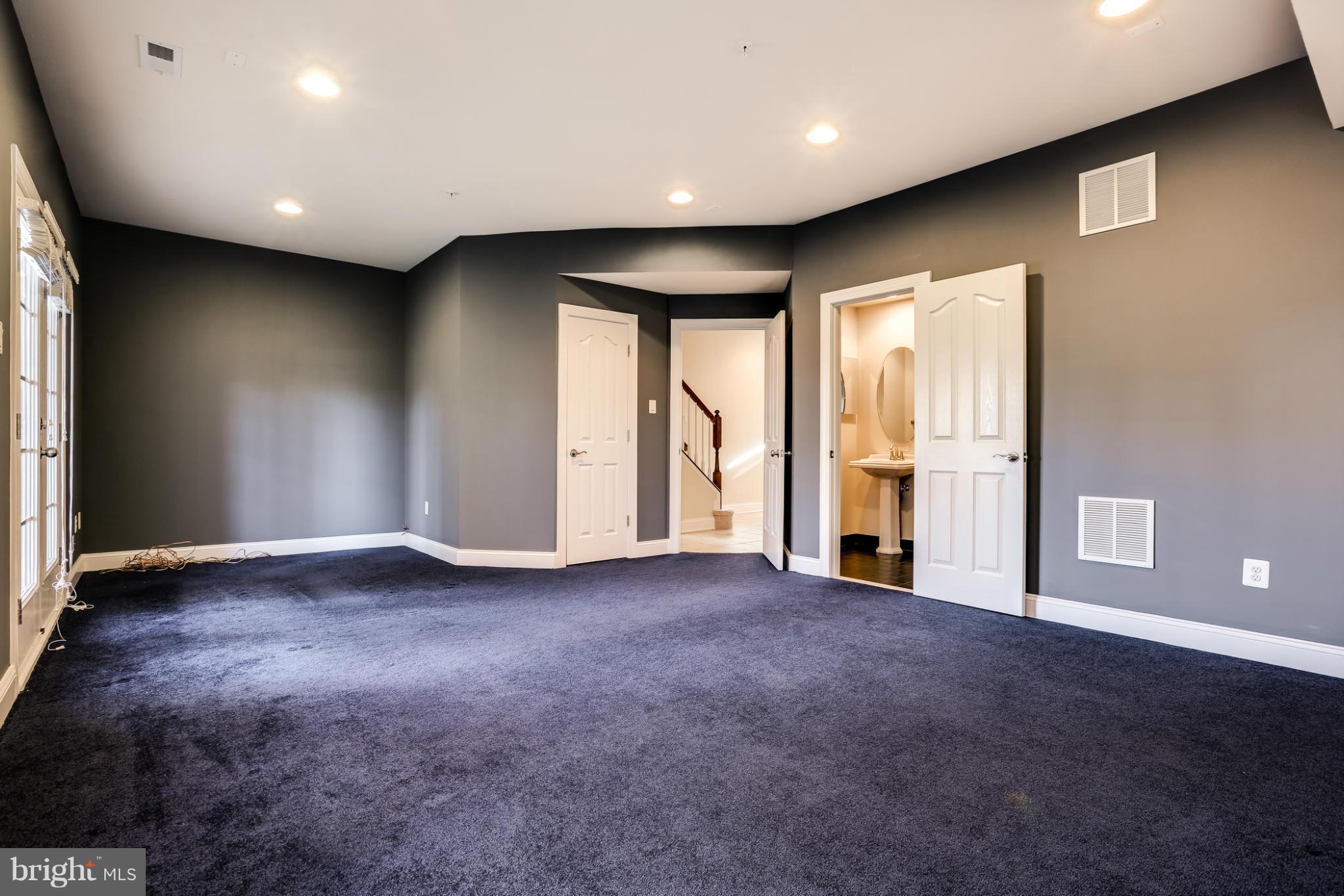 Empty carpeted room with dark gray walls, windows, and open doors to a hallway and bathroom.