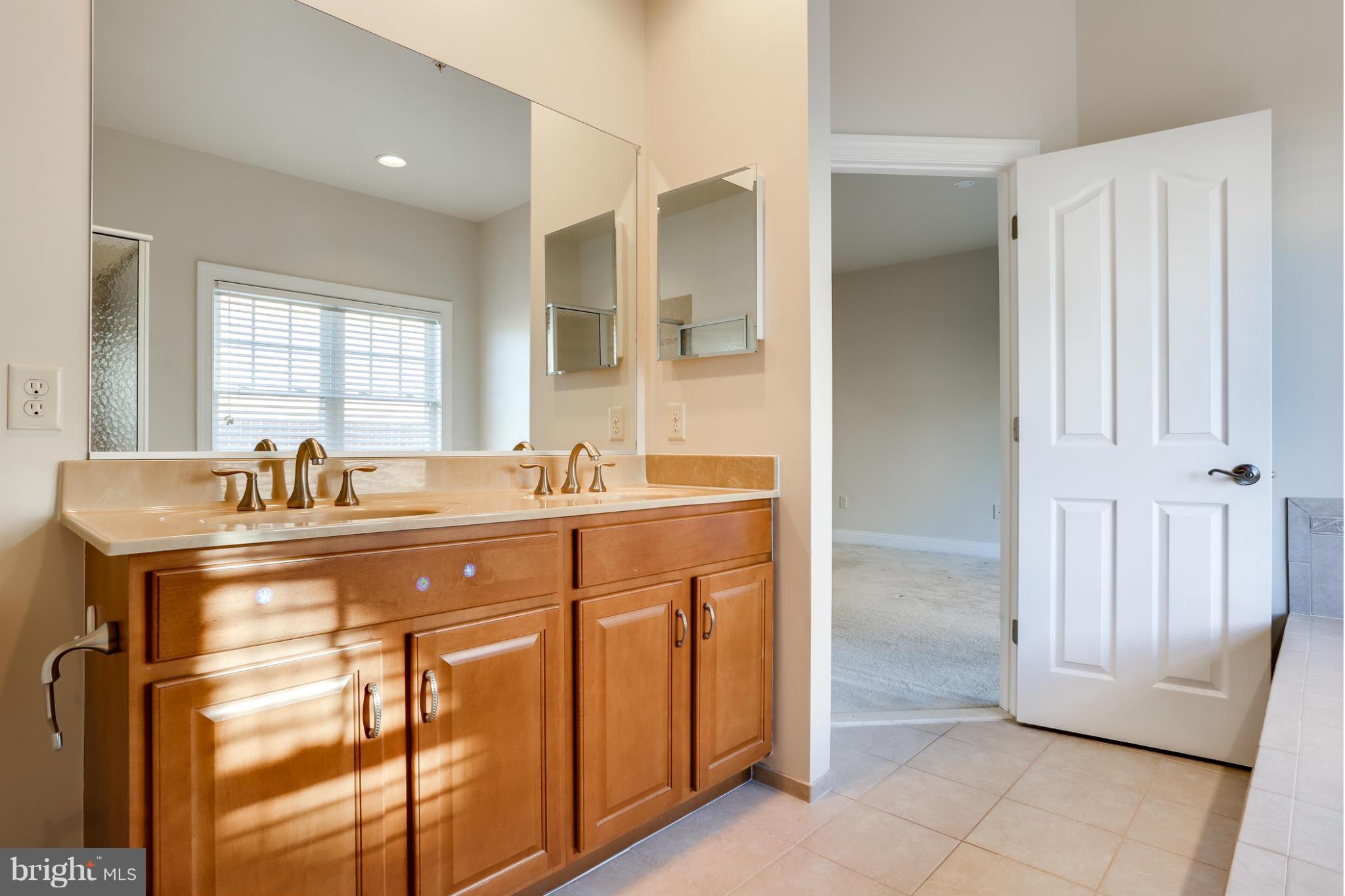 Bathroom with a double-sink wood vanity, large mirror, and open door to a carpeted room.