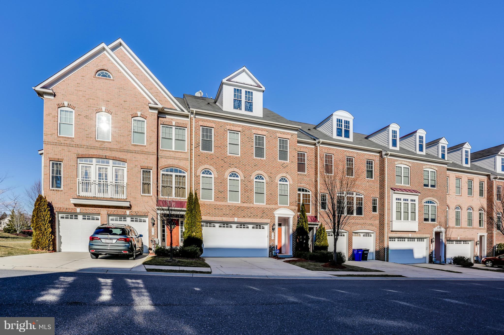 Brick townhouse with white dormers, an attached garage, and an orange front door.