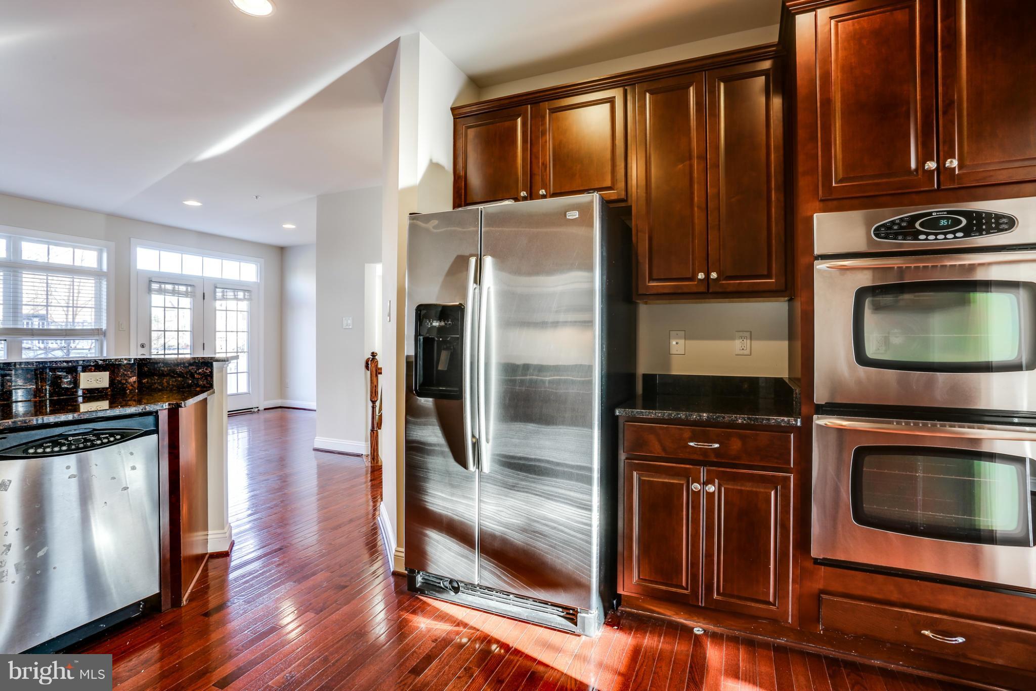 Kitchen with dark wood cabinets, granite counters, stainless steel appliances, and glossy hardwood floors.