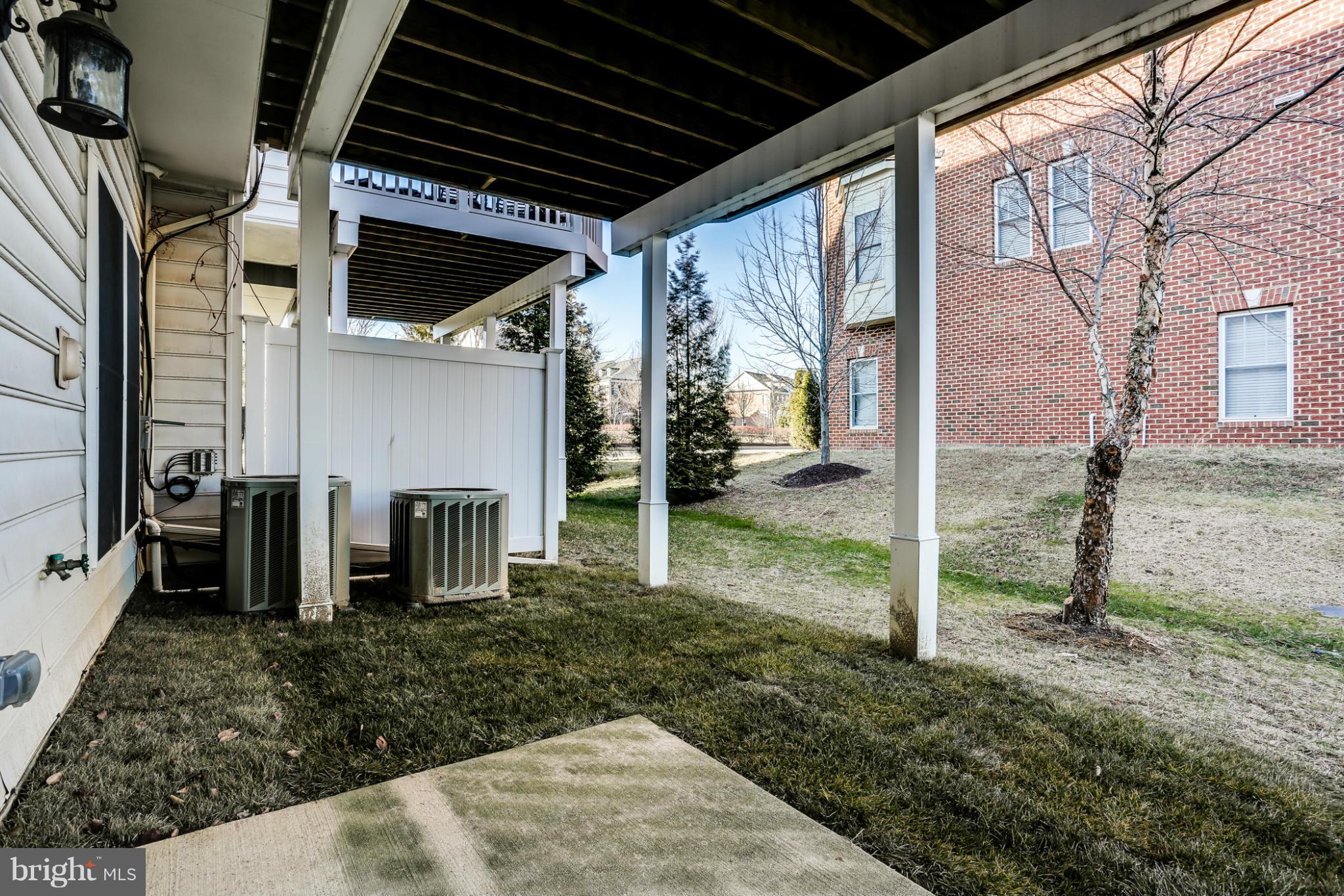 Covered backyard patio beneath an elevated deck, with air-conditioning units and a winter lawn.