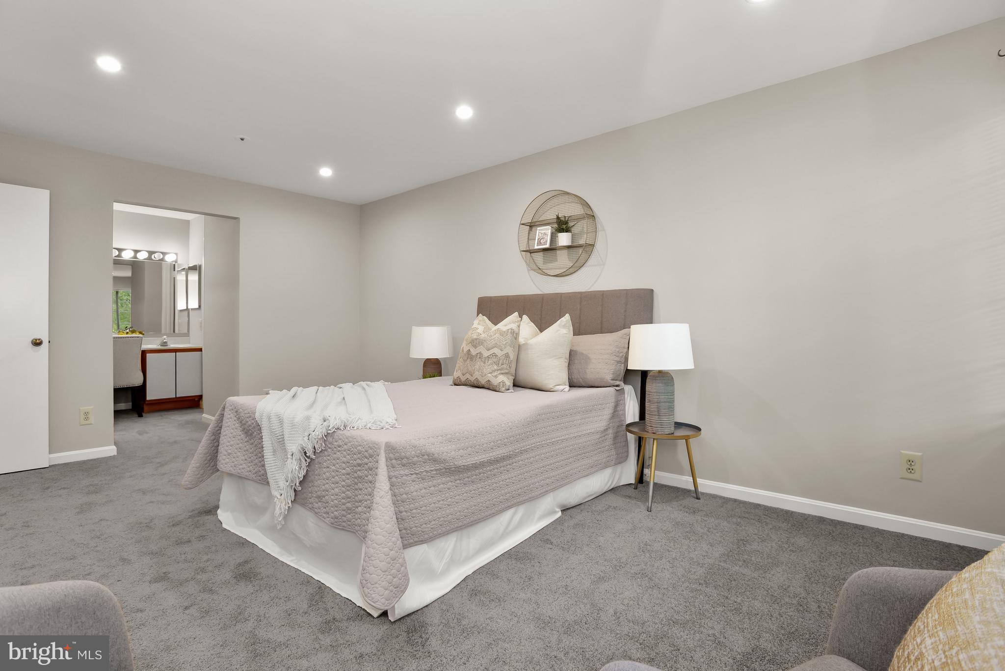Staged bedroom with pale quilted bedding, matching bedside lamps, and an open doorway to the bathroom.