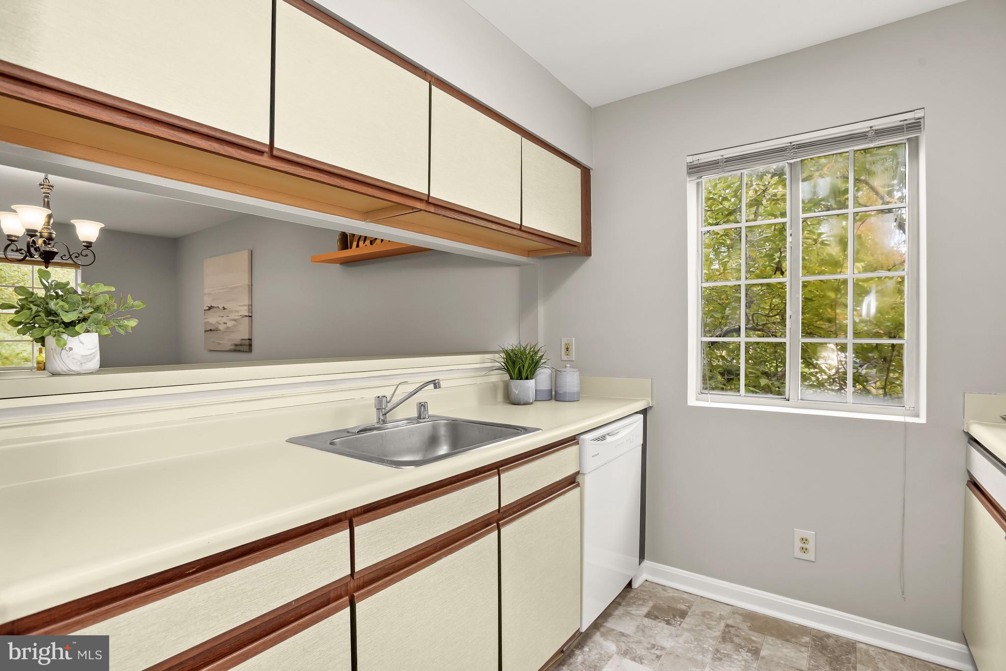 Kitchen with cream and wood-trimmed cabinetry, stainless-steel sink, and a large leafy-window view.