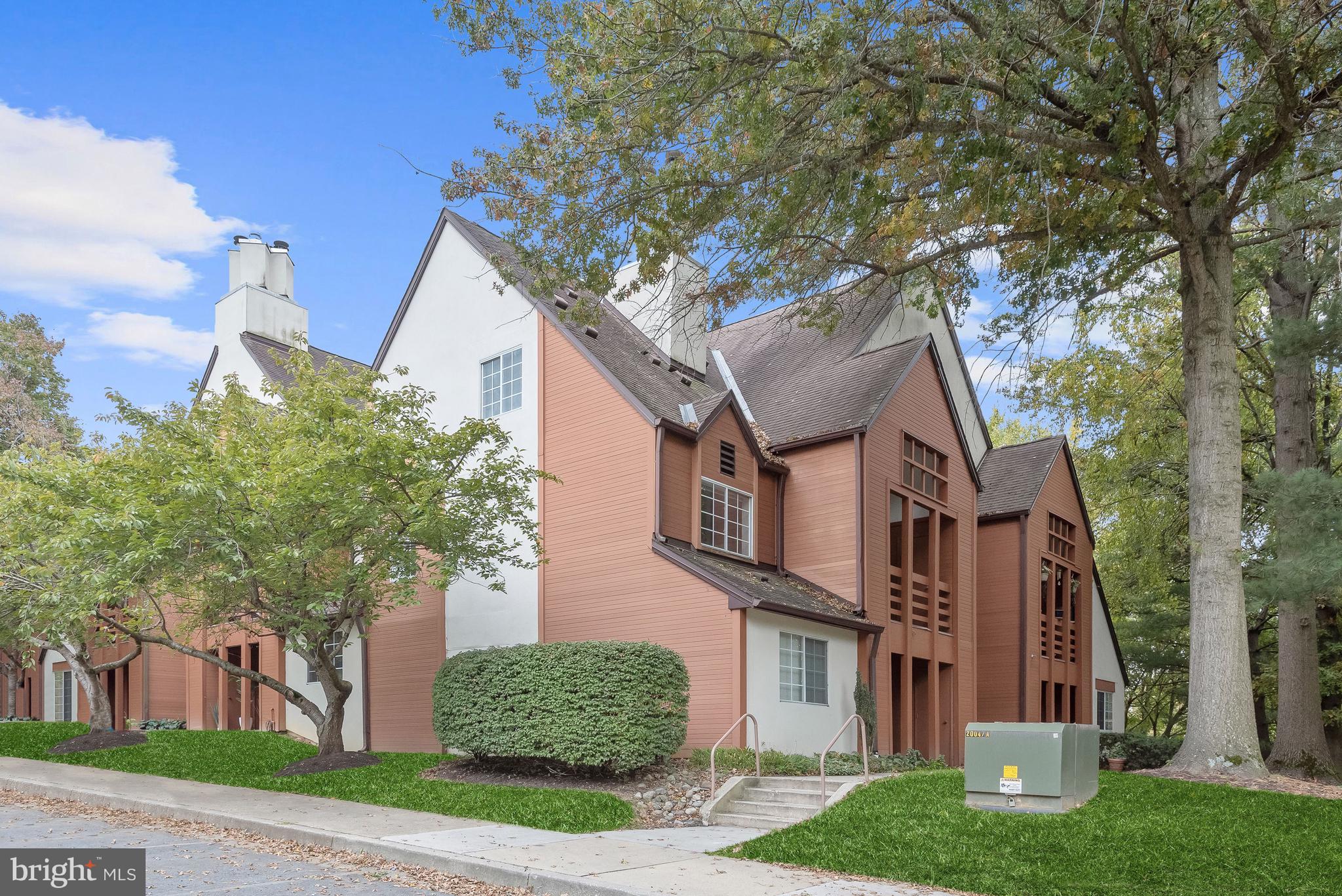 Multi-unit building with salmon siding, steep gabled roofs, mature trees, and landscaped grounds.