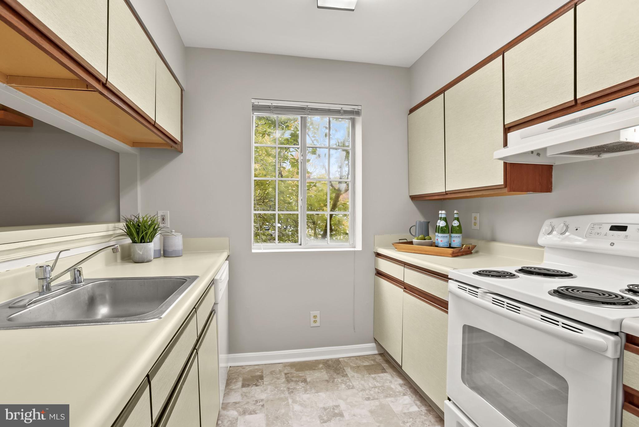 Kitchen with cream cabinets, wood trim, a white electric range, and a window overlooking leafy trees.