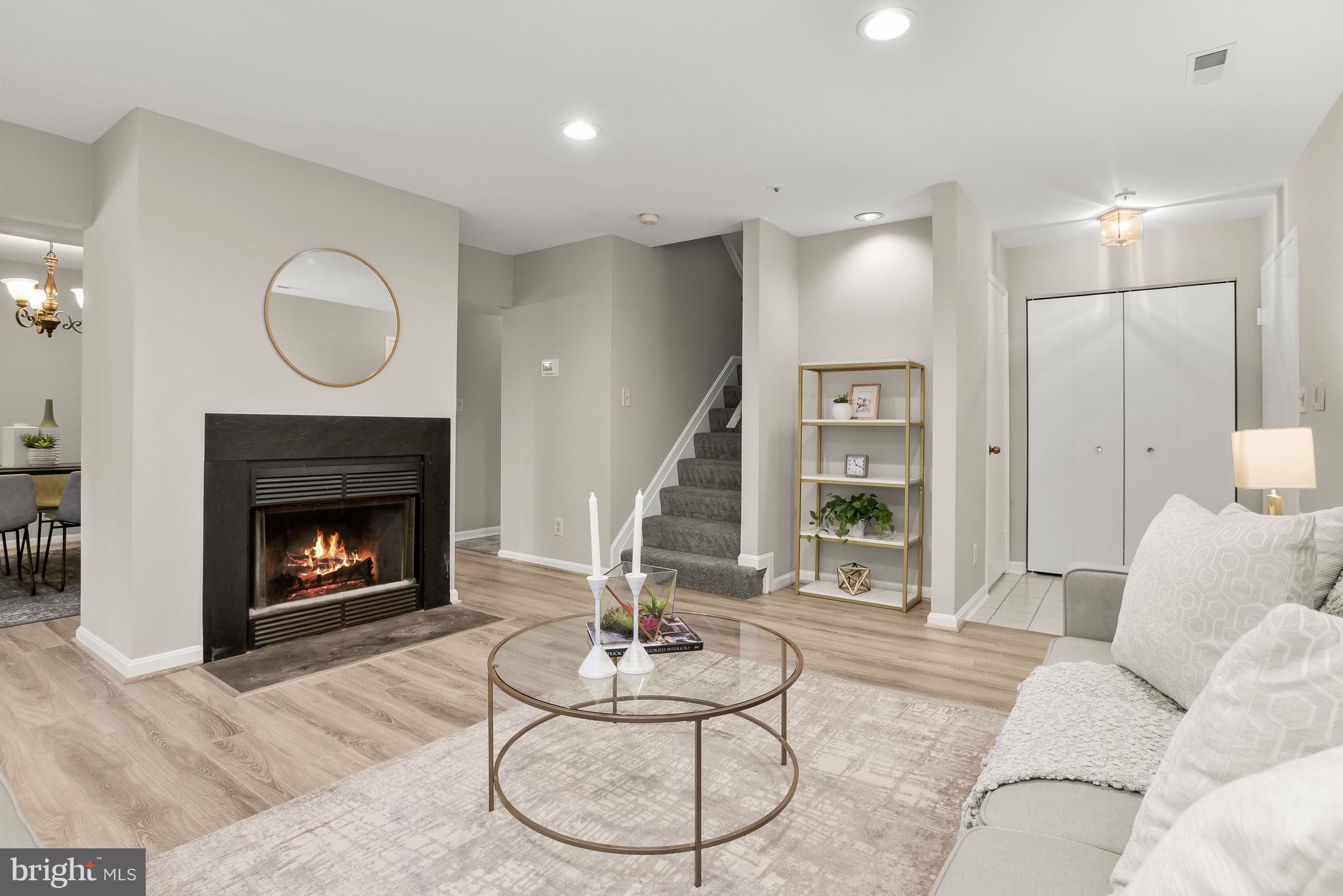 Staged living room with a lit fireplace, round coffee table, and staircase.