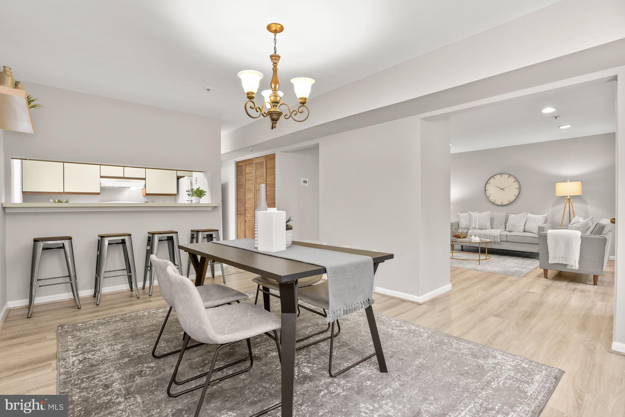 Open-plan dining area with a dark table and breakfast bar, adjoining a gray furnished living room.