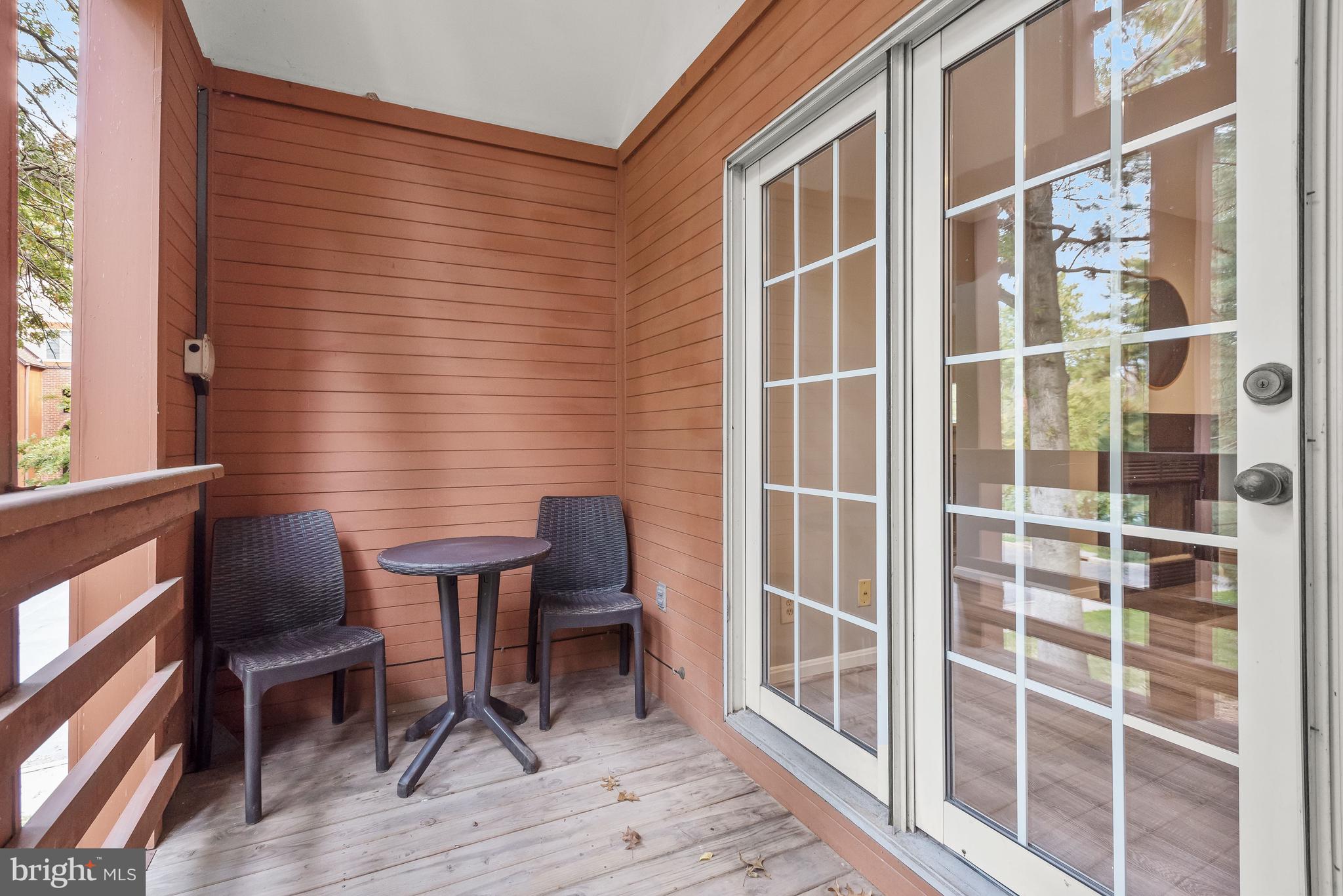 Covered balcony with two chairs and a small table beside white grid-pane sliding glass doors.