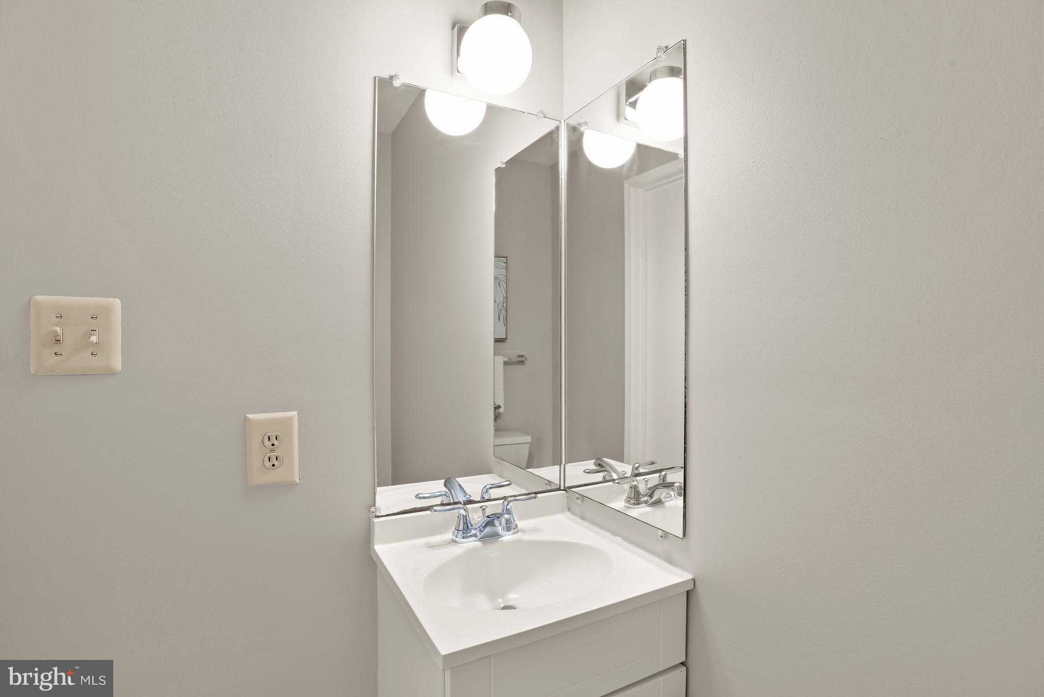 Bathroom vanity with a white sink, chrome faucets, and large mirrored panels.