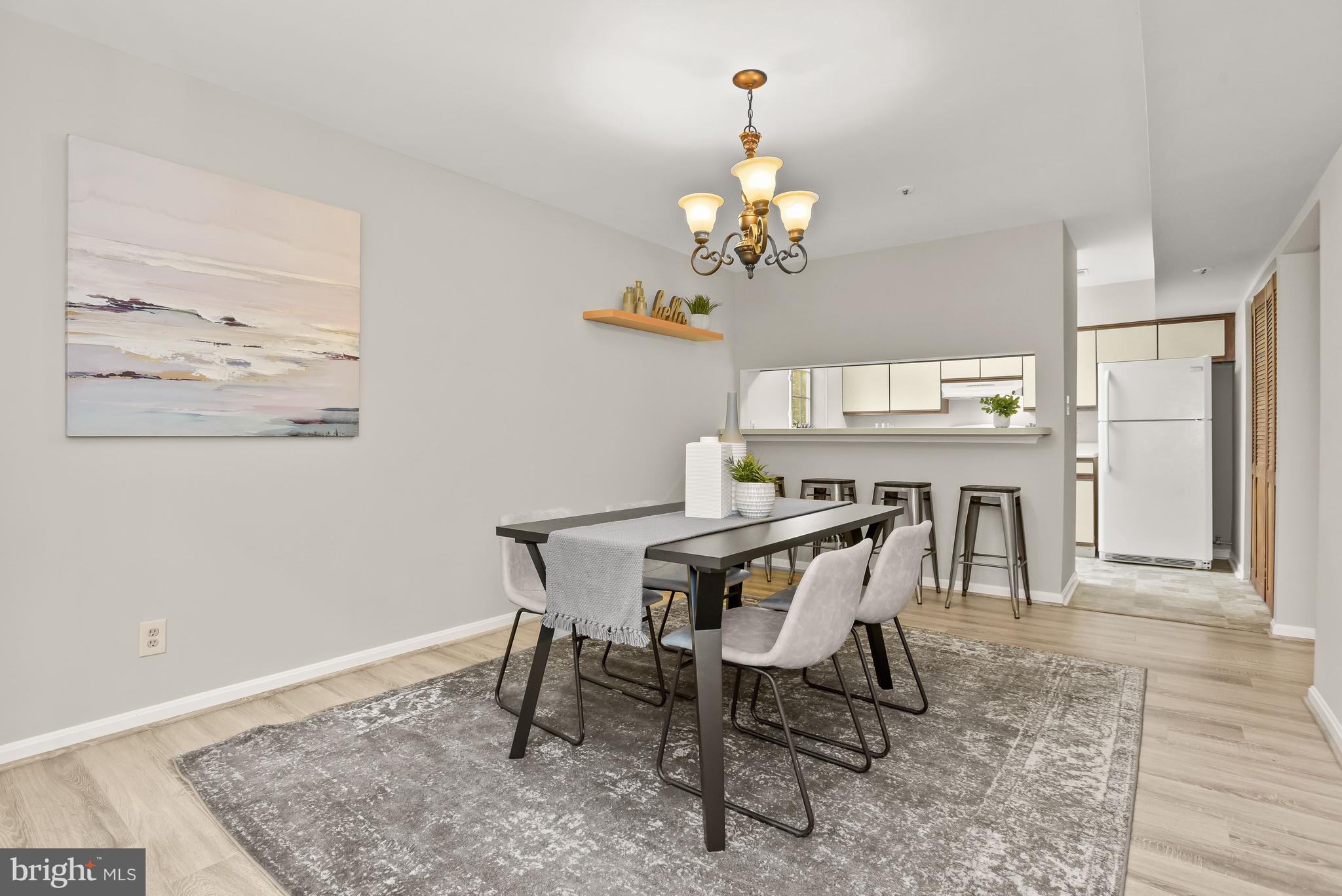 Staged dining room with a dark table, upholstered chairs, brass chandelier, and kitchen pass-through.