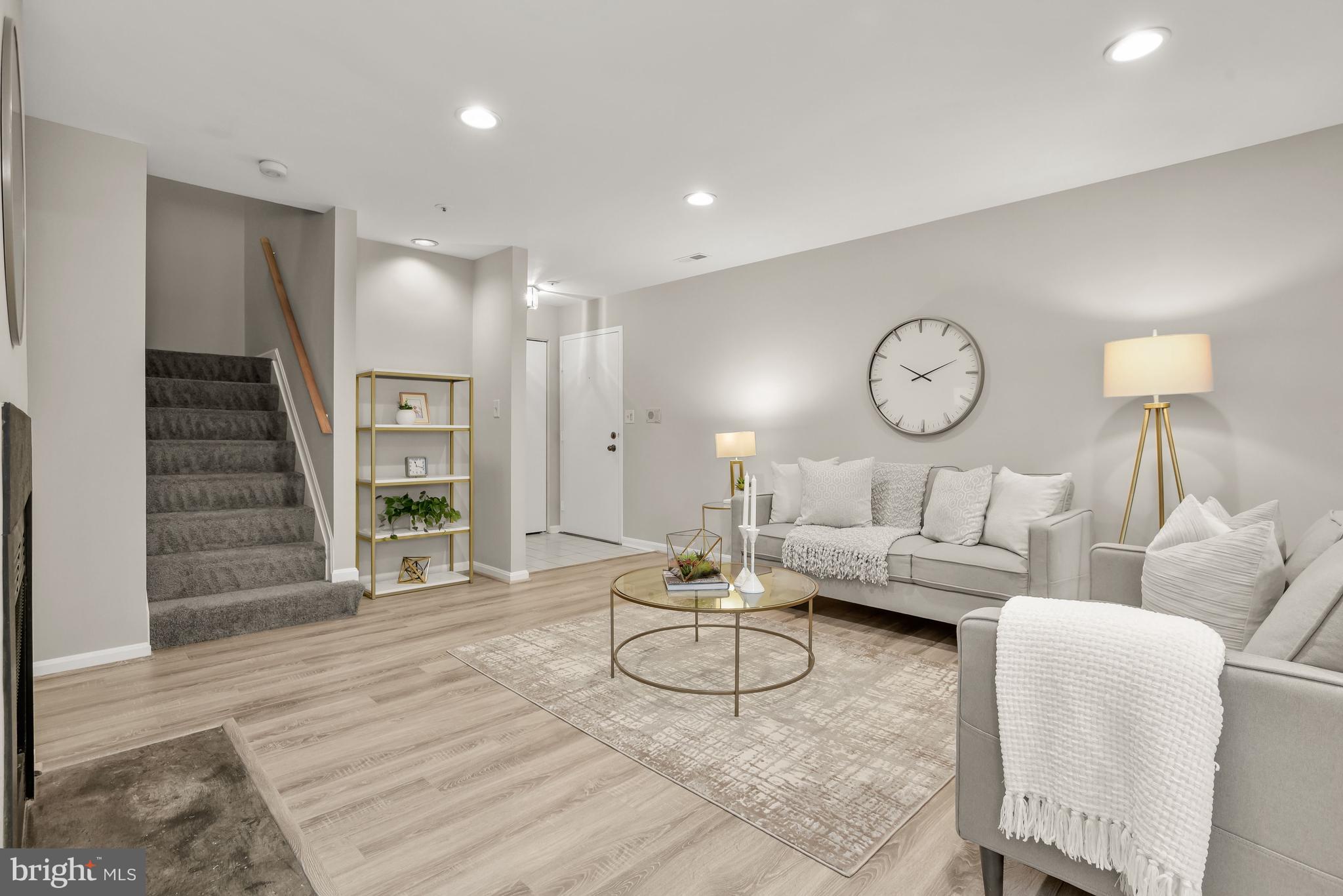 Staged living room with gray sofas, a glass coffee table, and carpeted stairs.