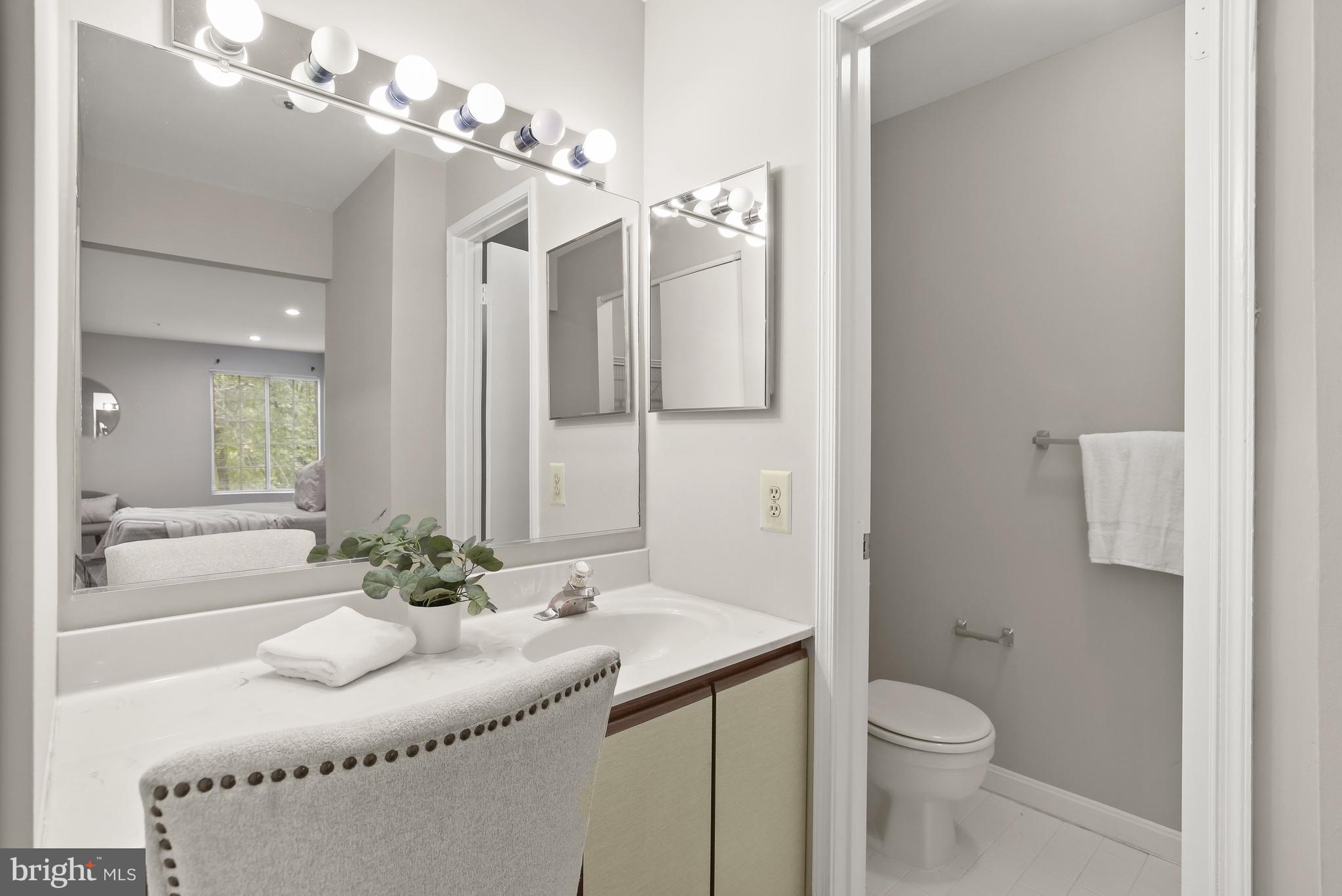 Bathroom vanity with bright mirror lights, a marble-look counter, and a separate toilet alcove.