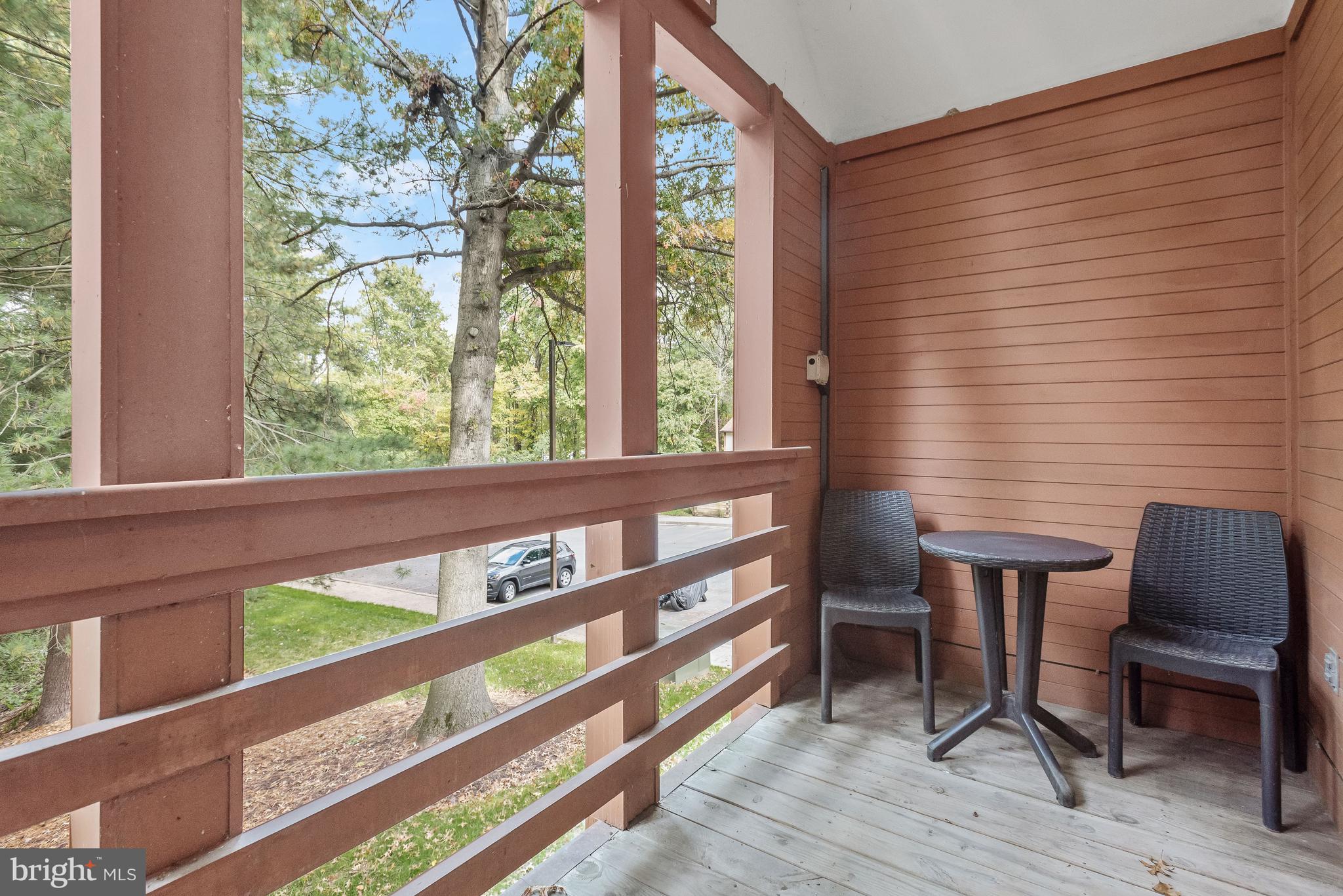 Covered balcony with two woven chairs and a small table overlooking trees and lawn.