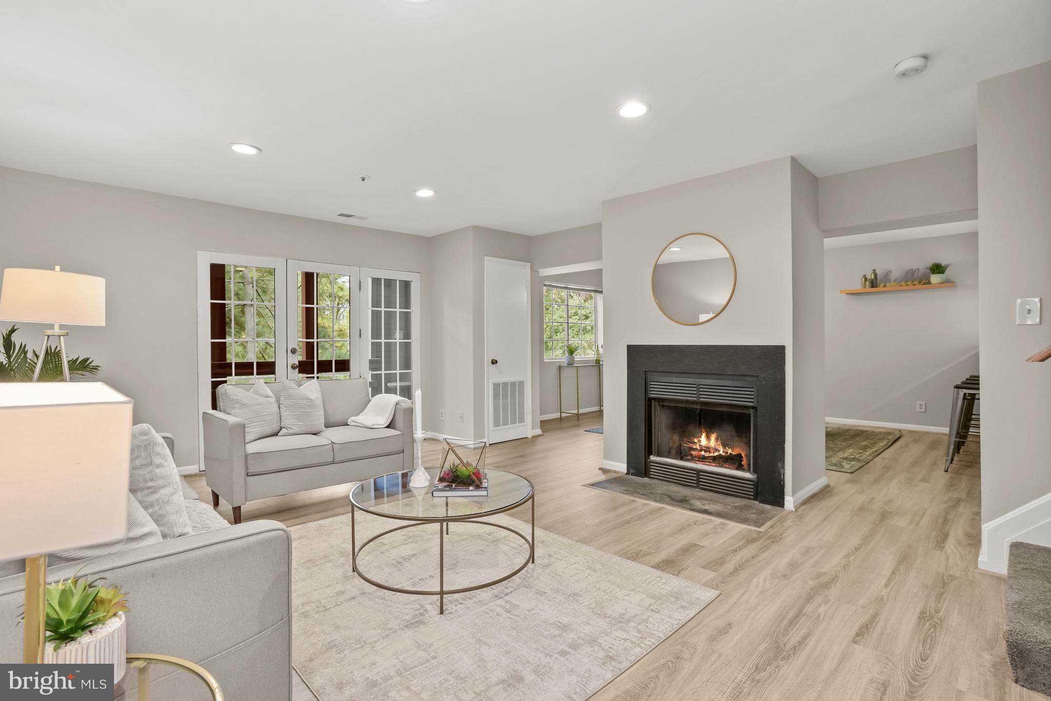 Living room with a lit fireplace, gray sofa, glass coffee table, and French doors.