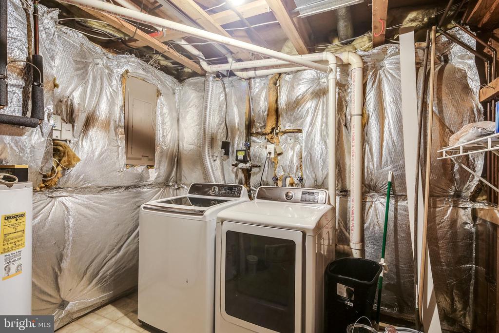 Basement laundry area with a washer and dryer amid exposed insulation and plumbing.
