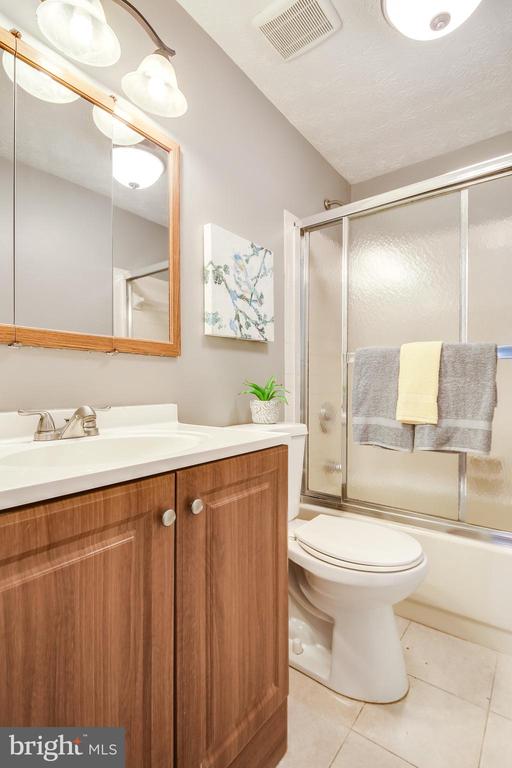 Bathroom with a wood vanity and frosted-glass tub and shower enclosure.