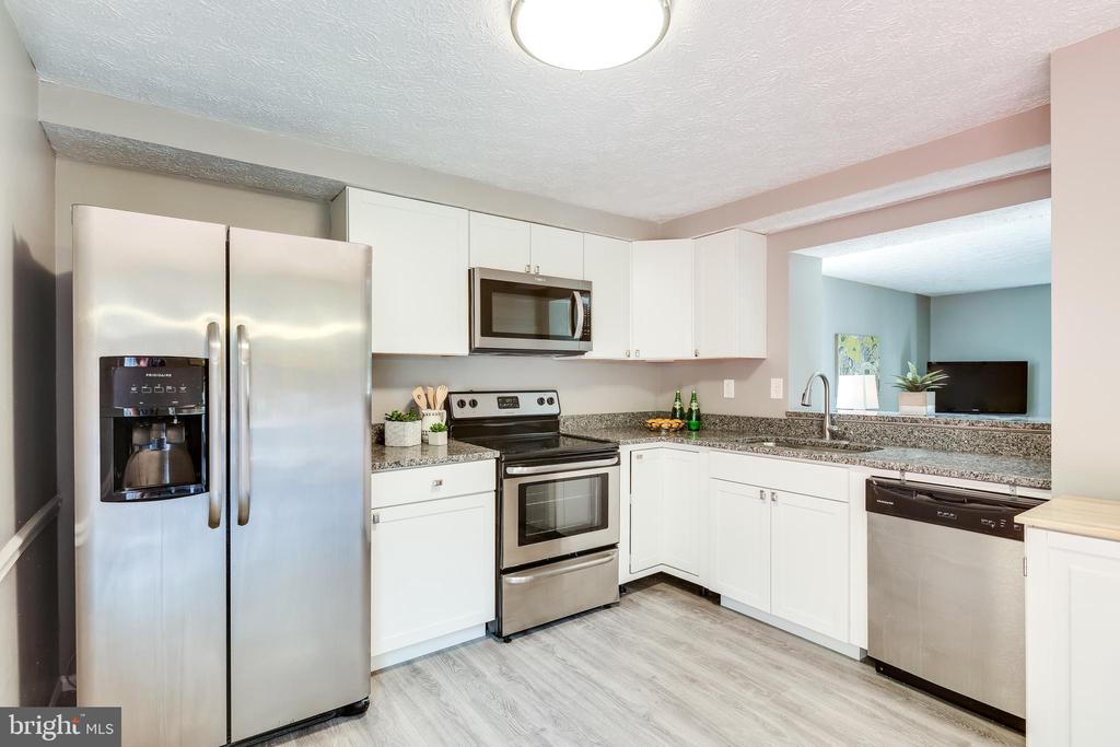 Kitchen with white cabinets, granite counters, stainless steel appliances, and a pass-through to the adjoining room.