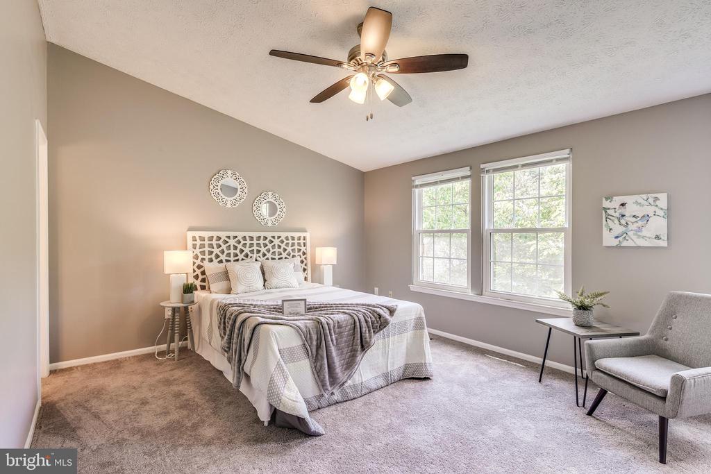 Staged bedroom with a patterned white headboard, two bright windows, and a gray accent chair.