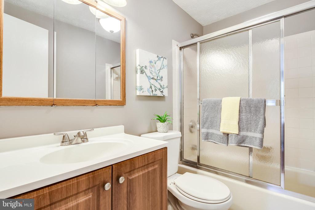 Bathroom with a wood vanity, white sink, toilet, and frosted-glass tub-shower enclosure.