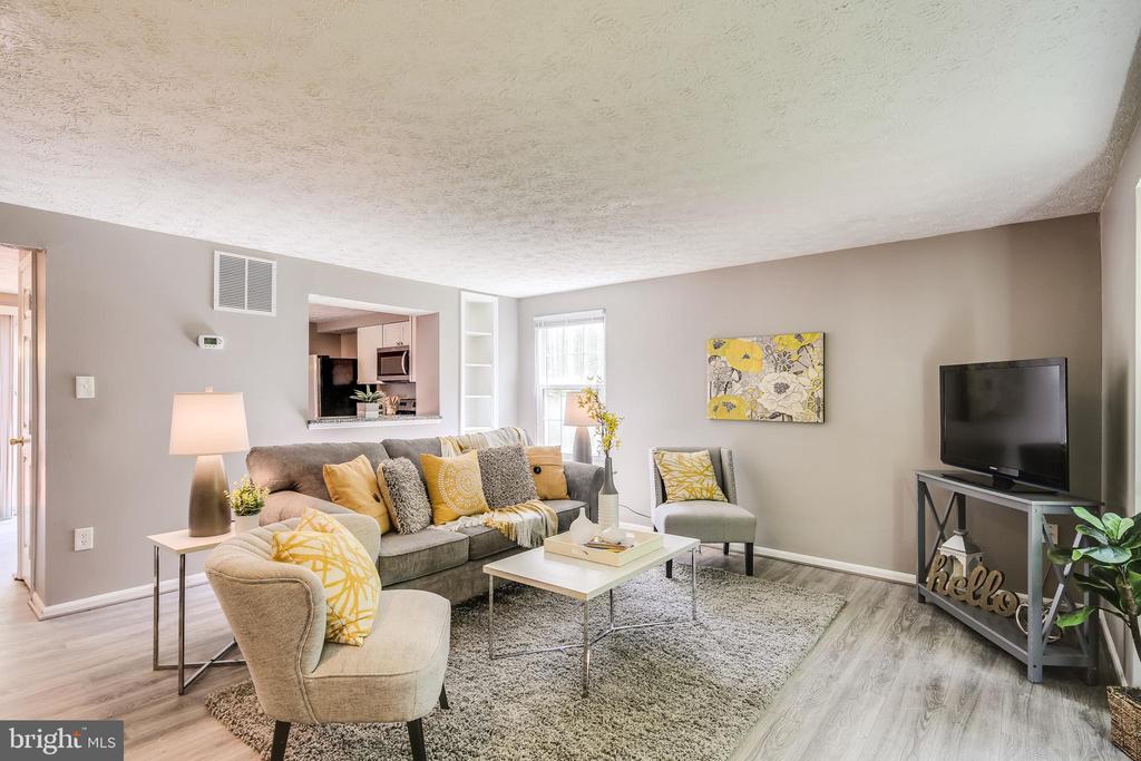Staged living room with a gray sofa, yellow accents, and an open kitchen pass-through.