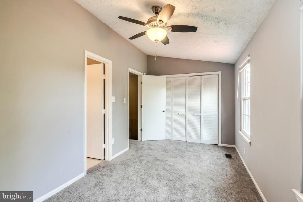 Empty bedroom with gray carpet, a ceiling fan, and white louvered closet doors.