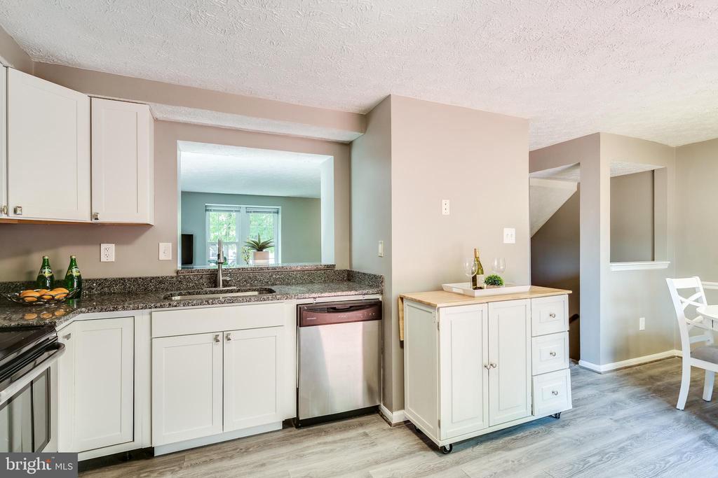 Kitchen with white cabinets, dark countertops, stainless dishwasher, and a small rolling island.